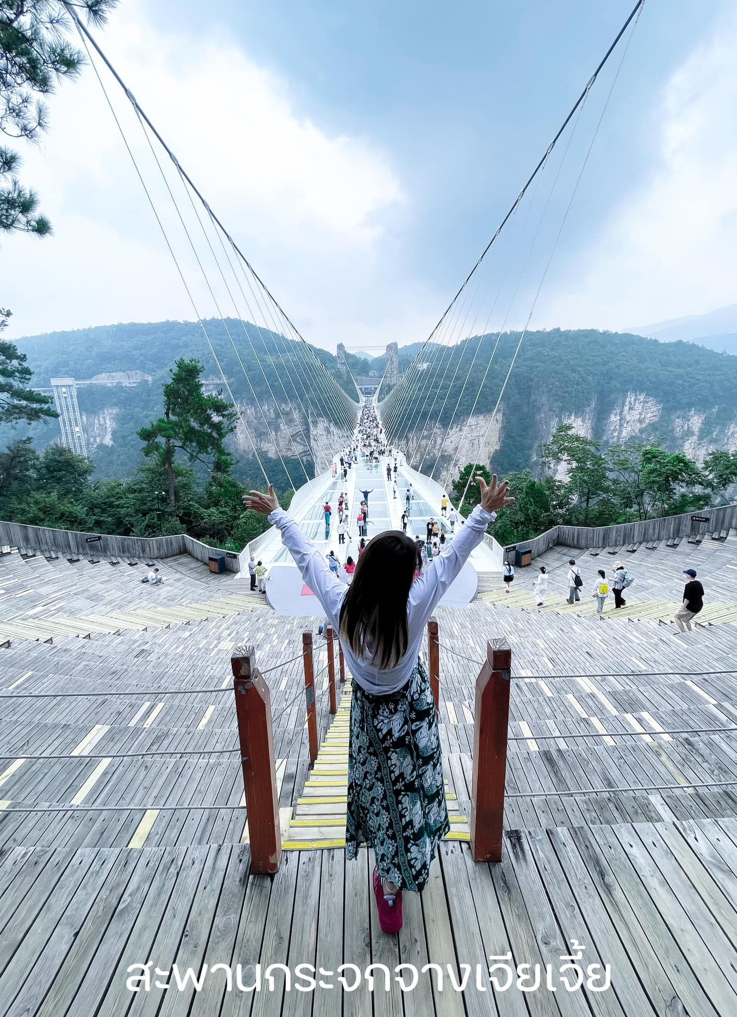 A woman is standing on a bridge with her arms outstretched.