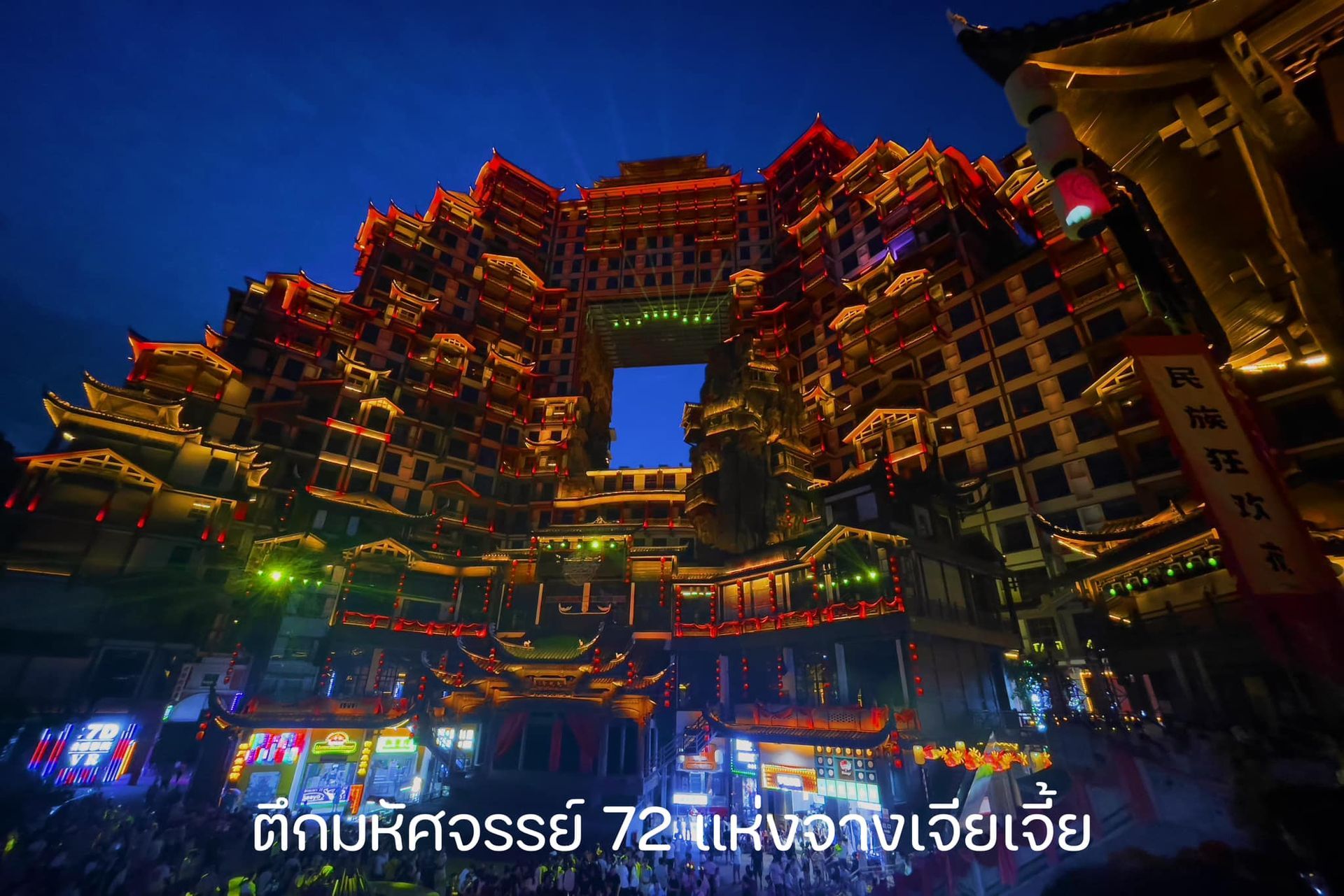 A large building with chinese writing on it is lit up at night.