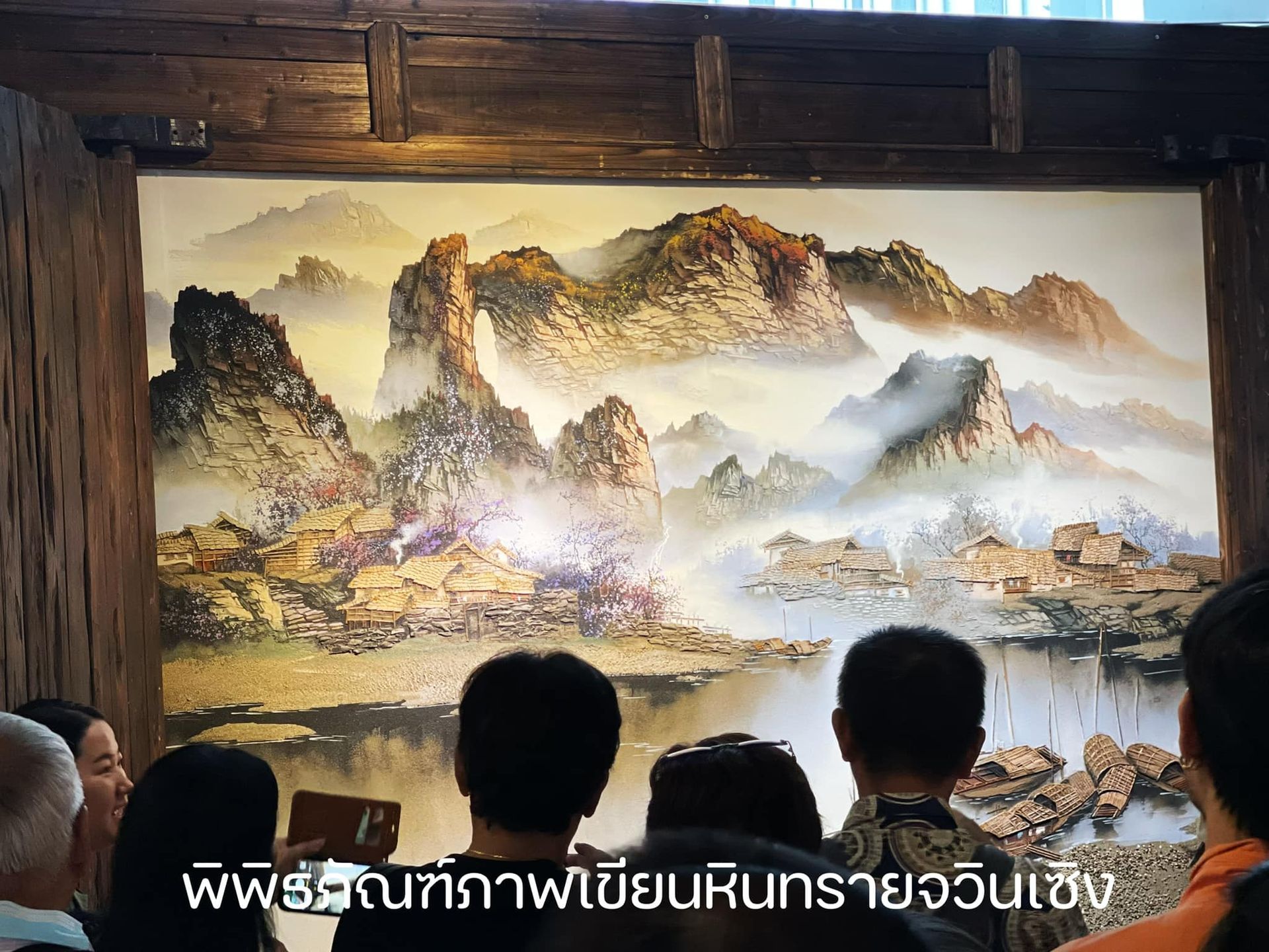 A group of people are looking at a painting of mountains and a river.