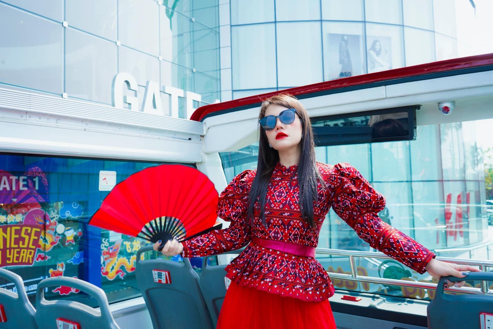 A woman in a red dress is holding a red fan in front of a building.