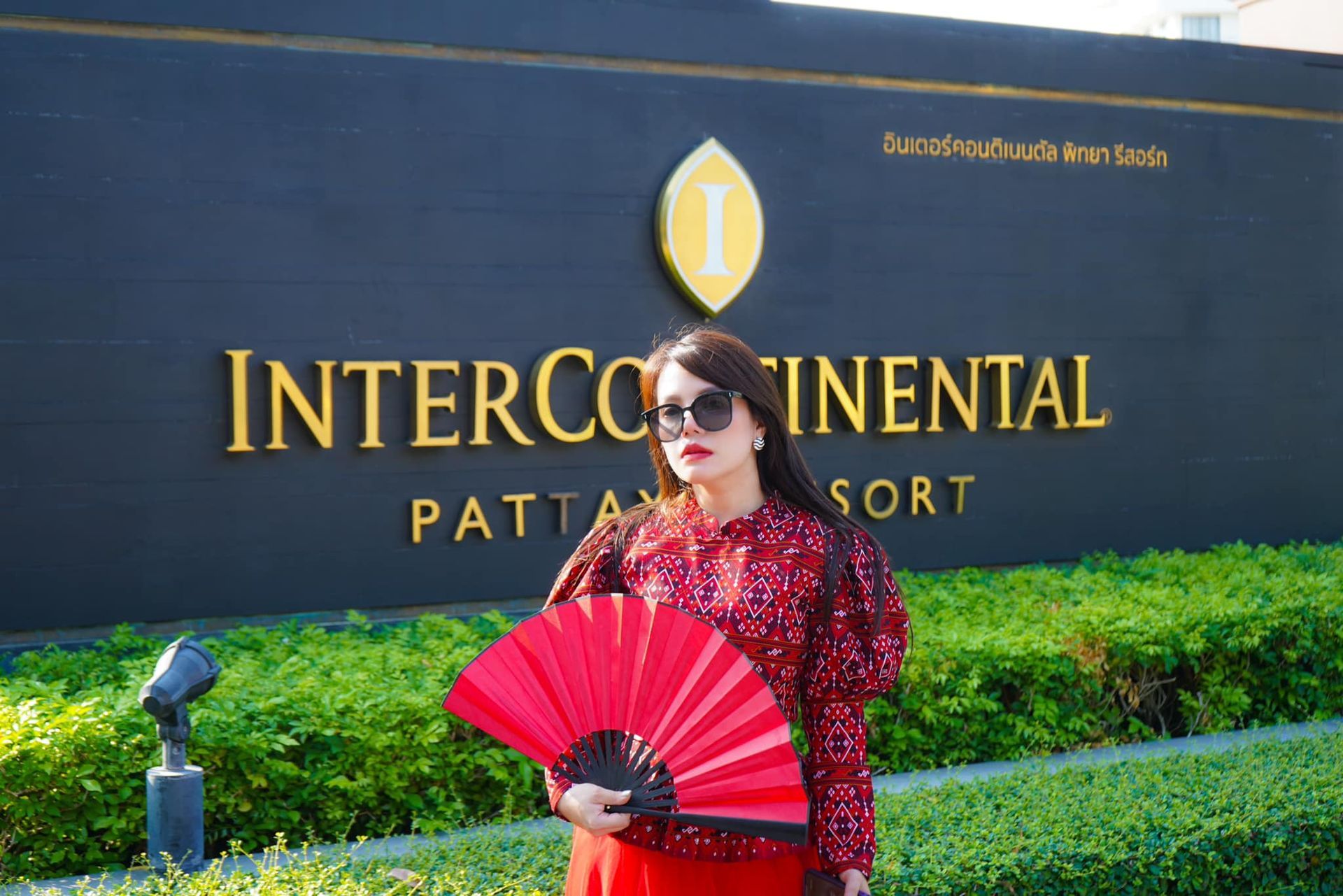 A woman is holding a red fan in front of a sign that says intercontinental