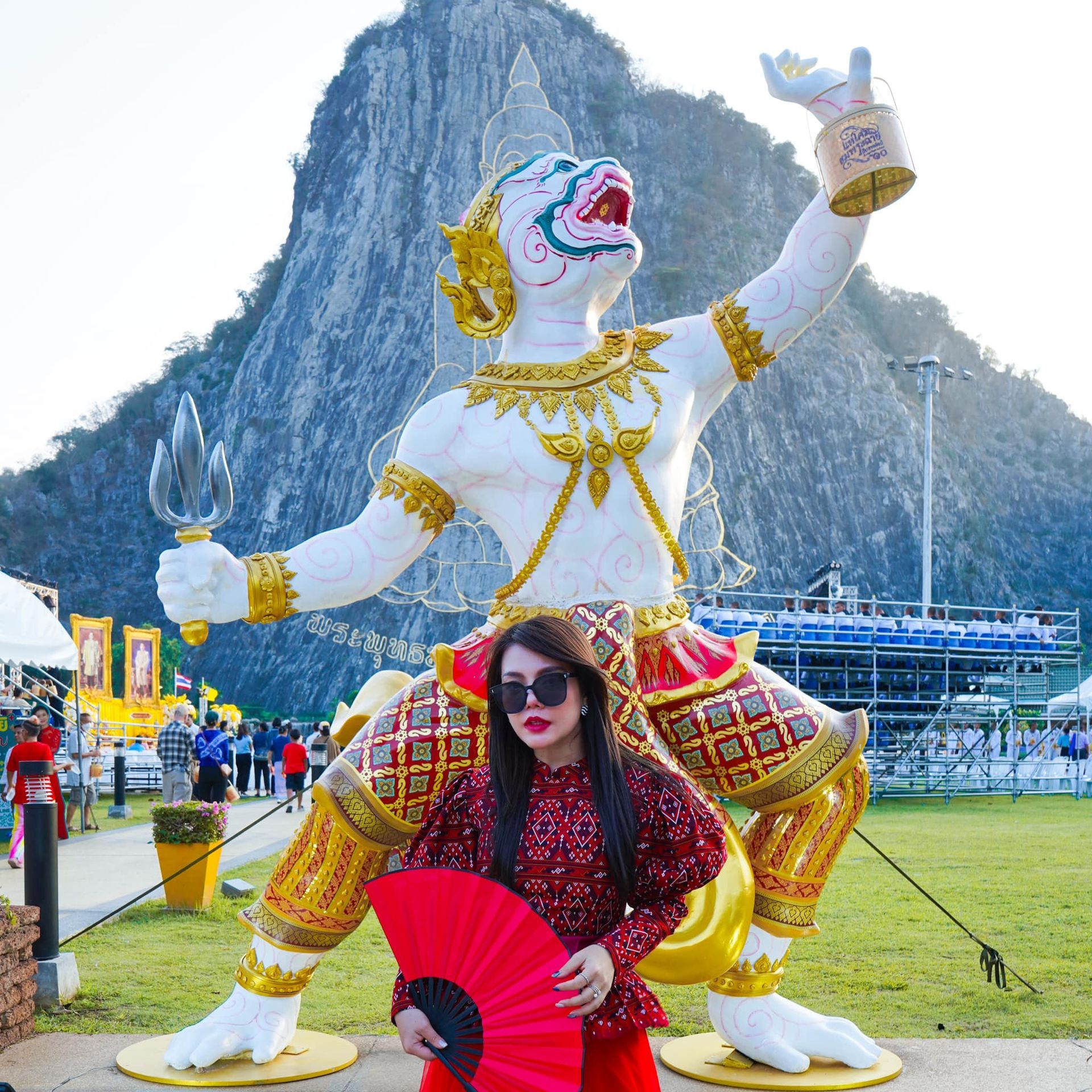 A woman is holding a red fan in front of a statue