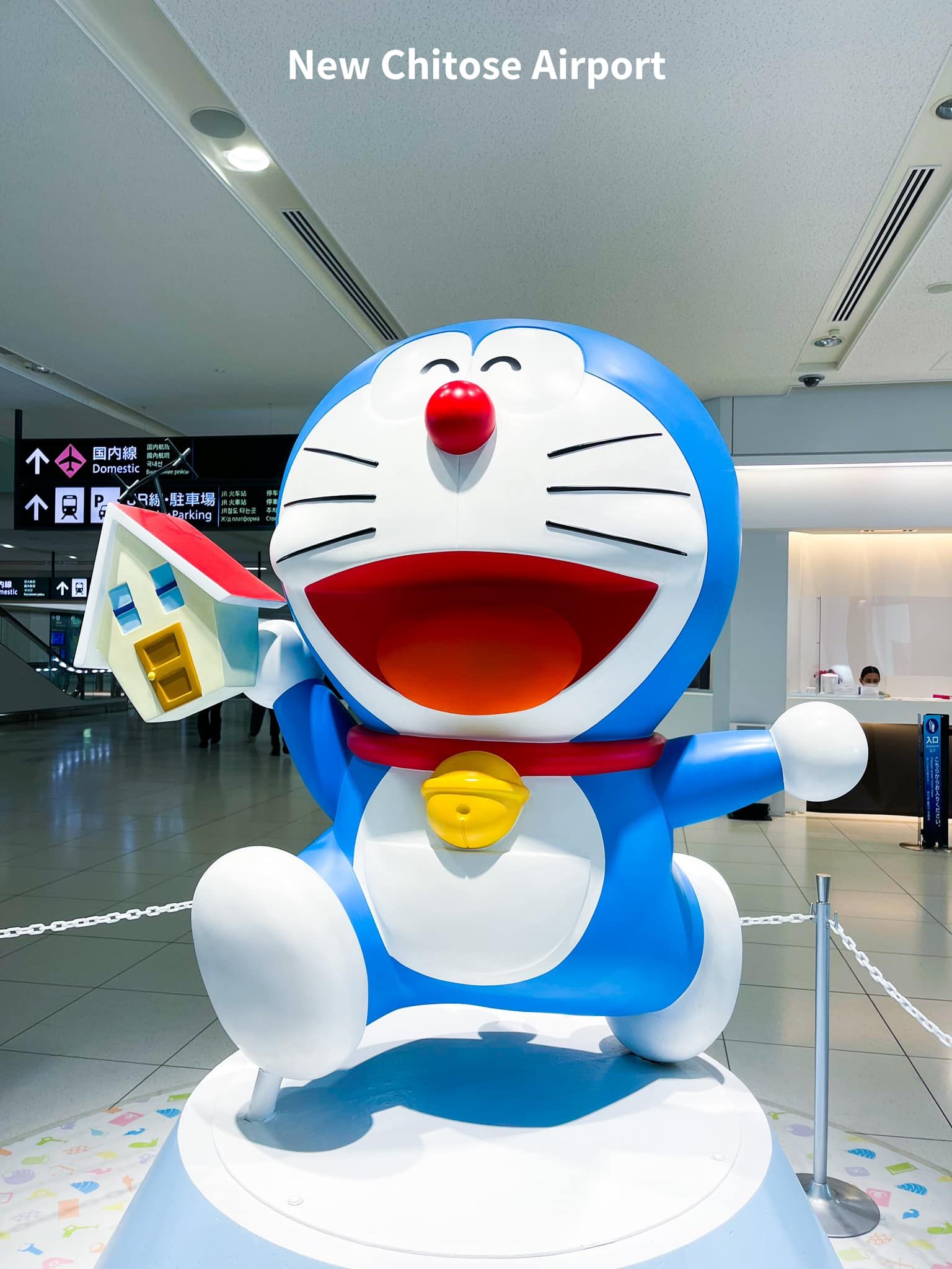 A statue of doraemon is holding a small house in his hand.