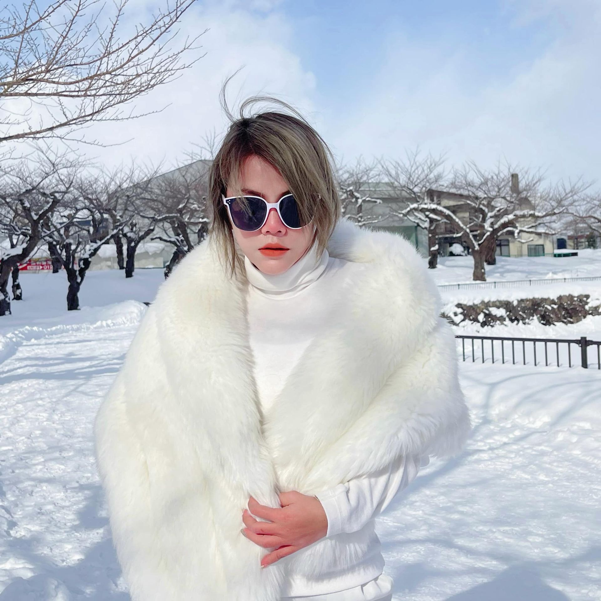 A woman wearing sunglasses and a white fur shawl is standing in the snow