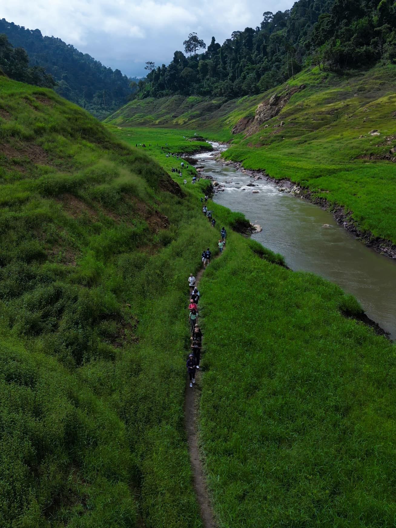 A group of people are walking down a path next to a river.