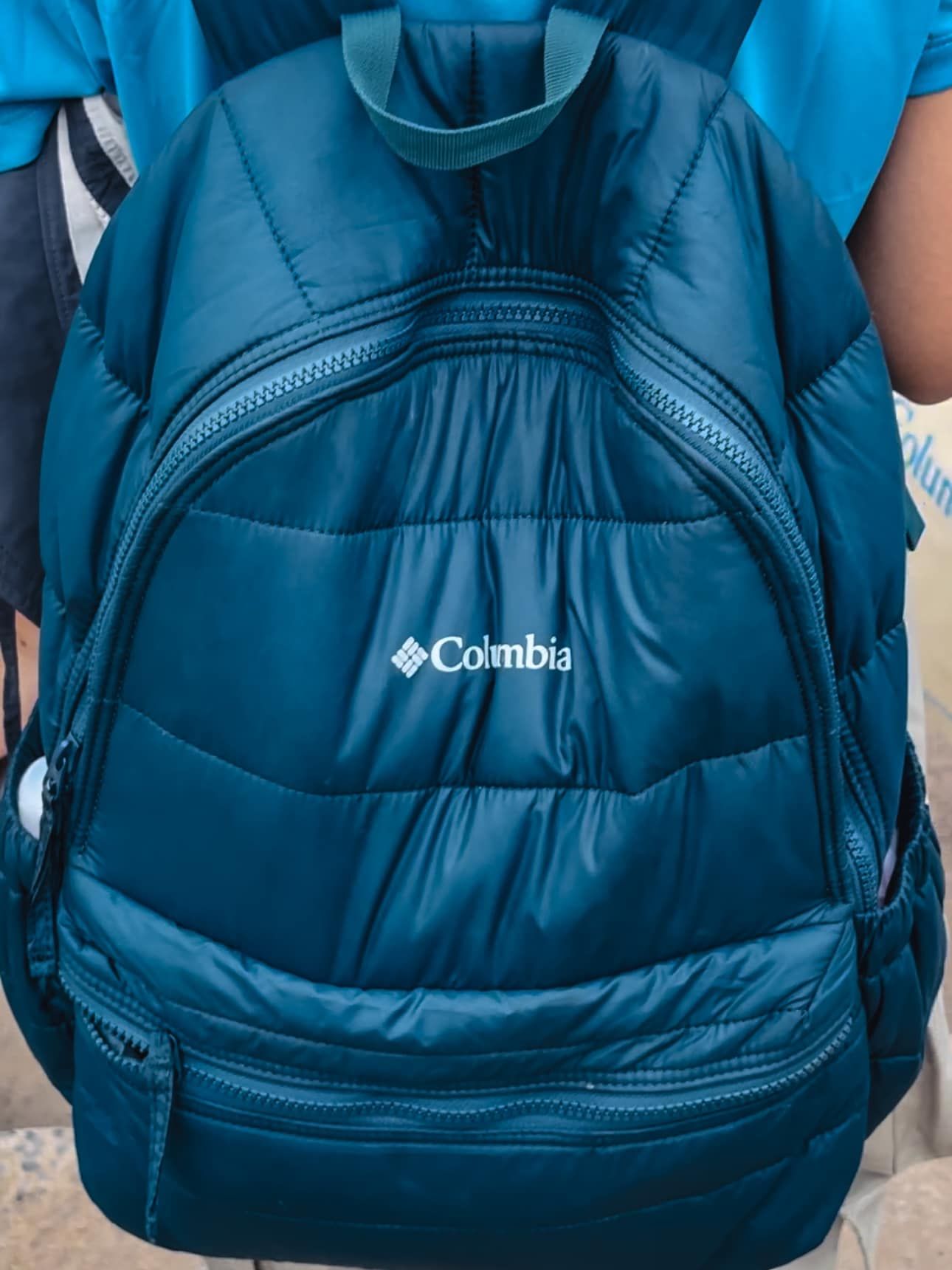 A person is carrying a blue columbia backpack on their back.