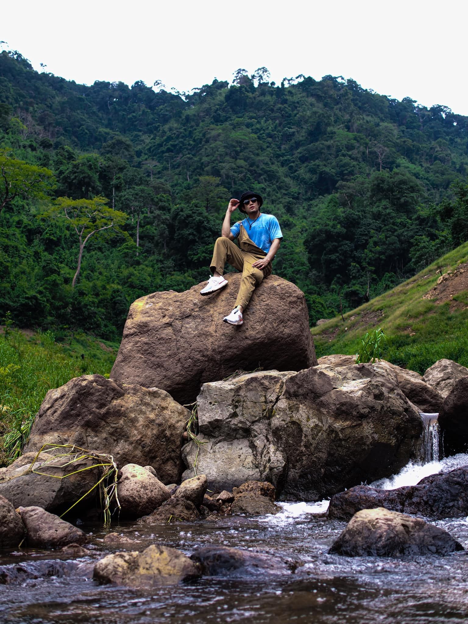 A man is sitting on a rock next to a river.