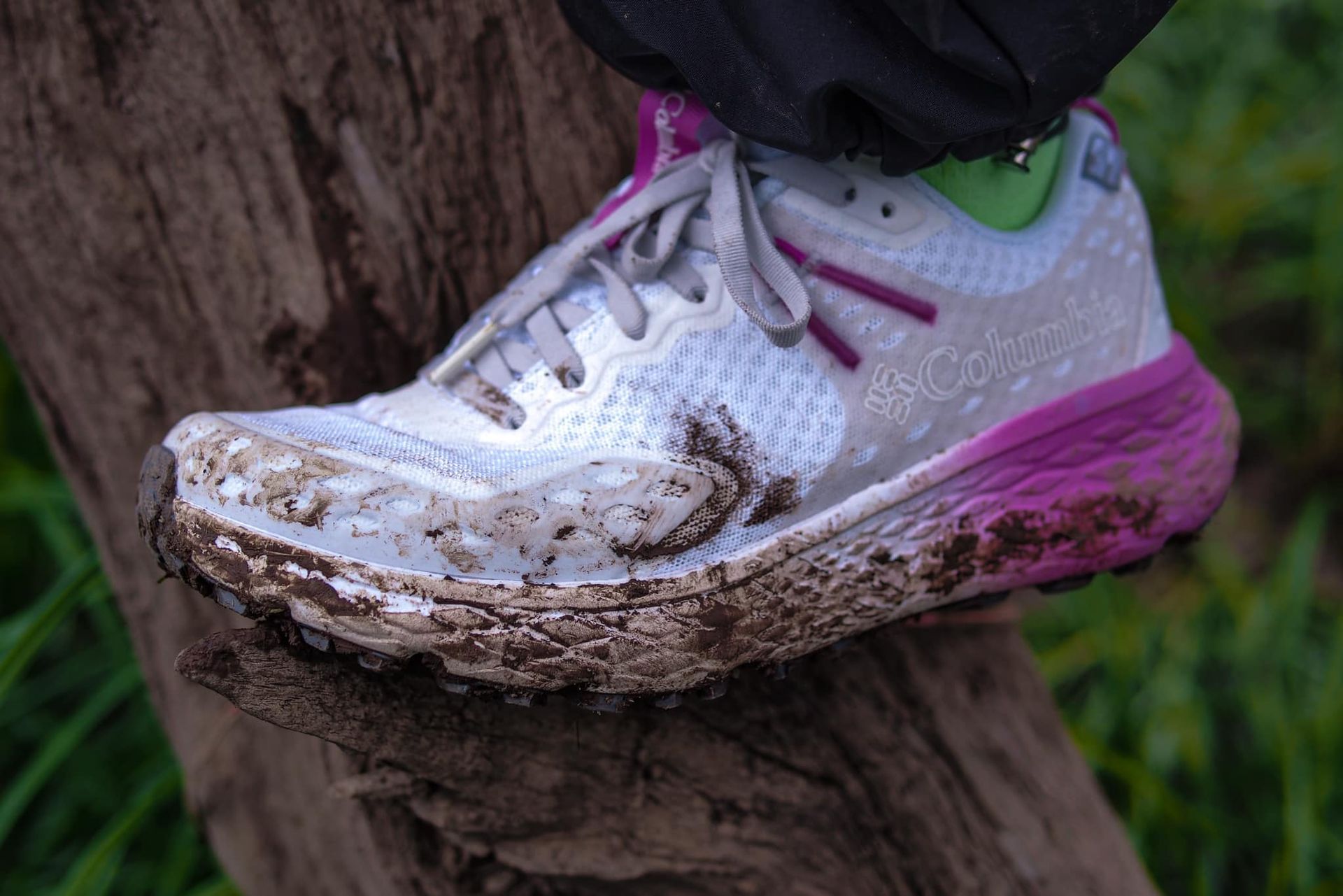 A person wearing a pair of muddy running shoes is standing on a tree trunk.