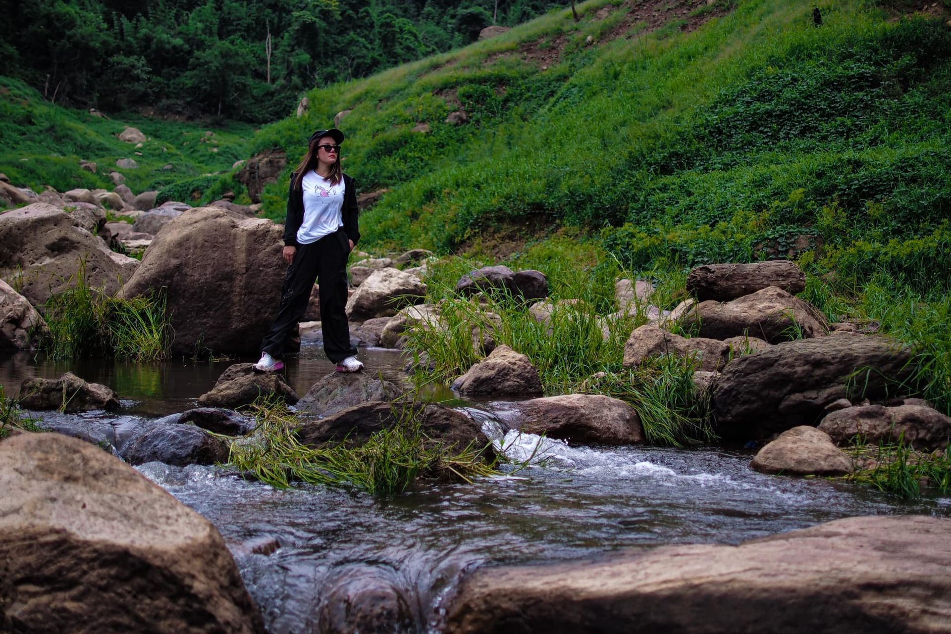 A woman is standing on a rock next to a river.