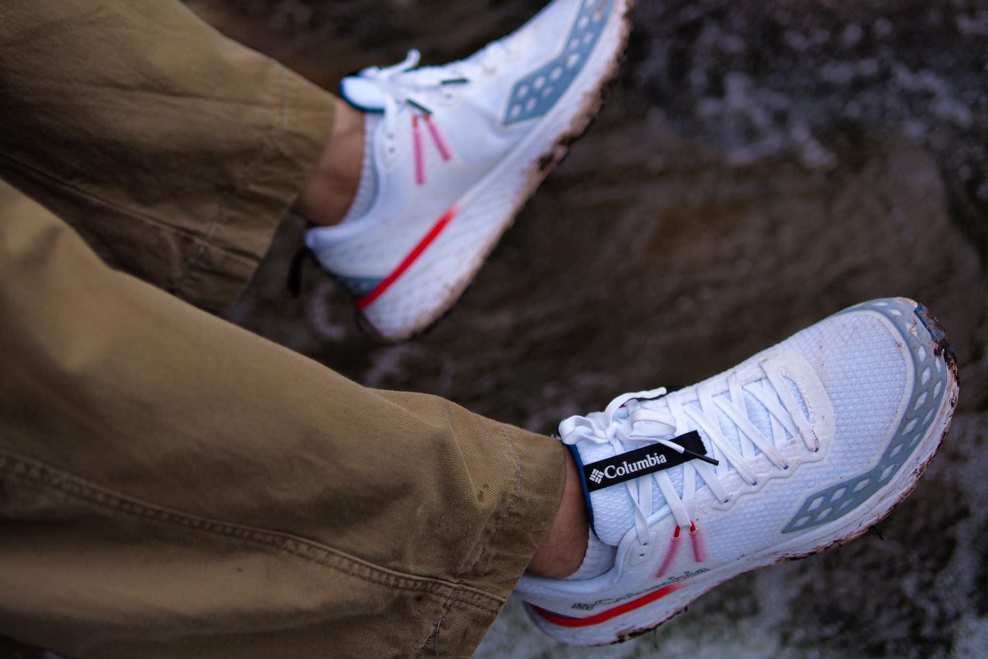 A person wearing a pair of white sneakers and khaki pants.