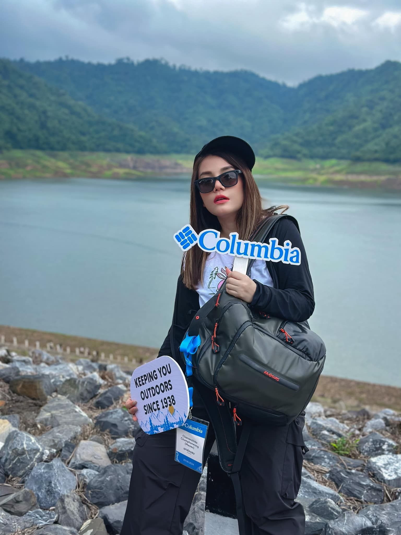 A woman is standing next to a lake holding a sign that says columbia.