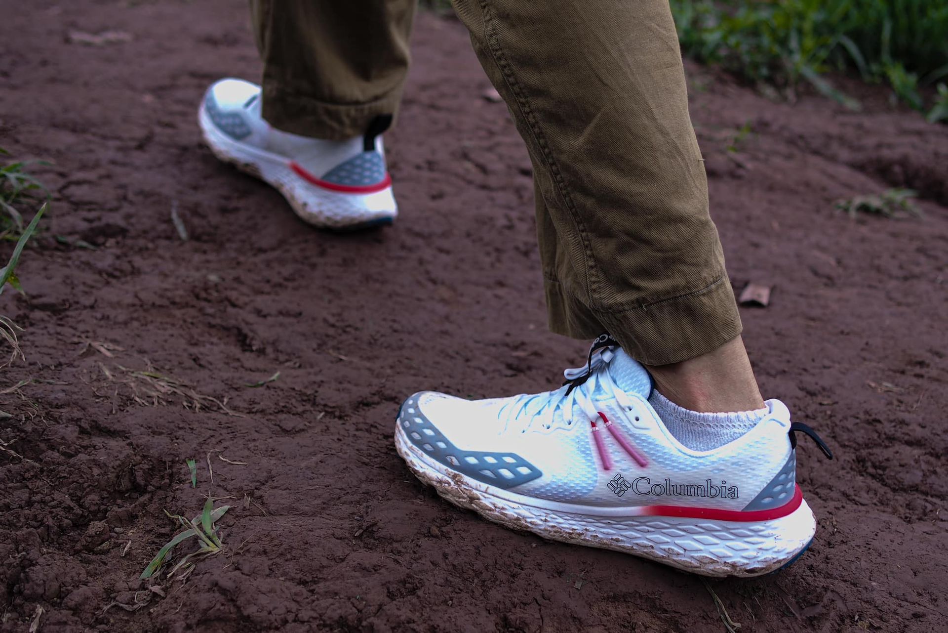 A person wearing a pair of white and red running shoes is walking on a dirt path.