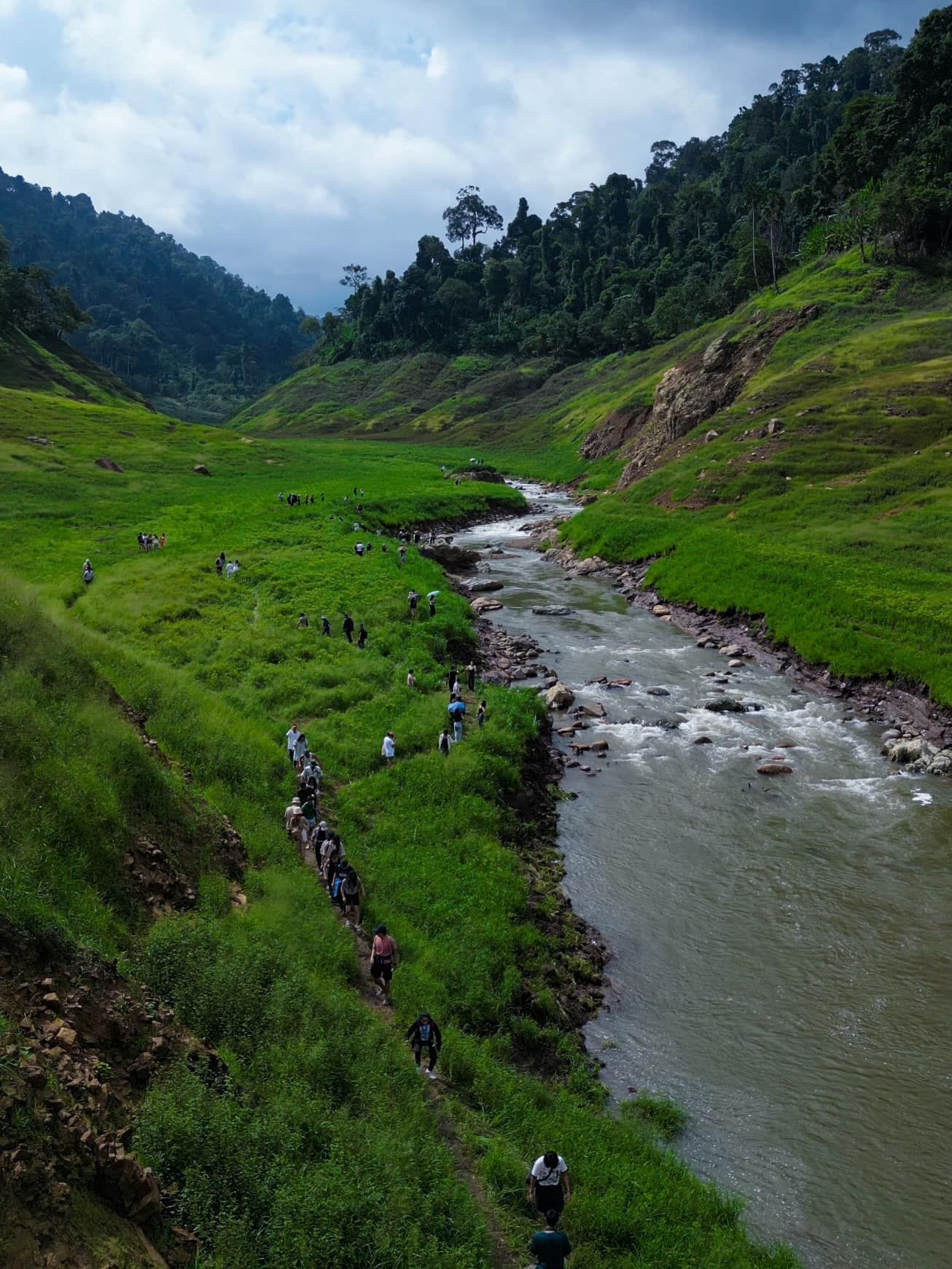 A group of people are walking along a river in the mountains.