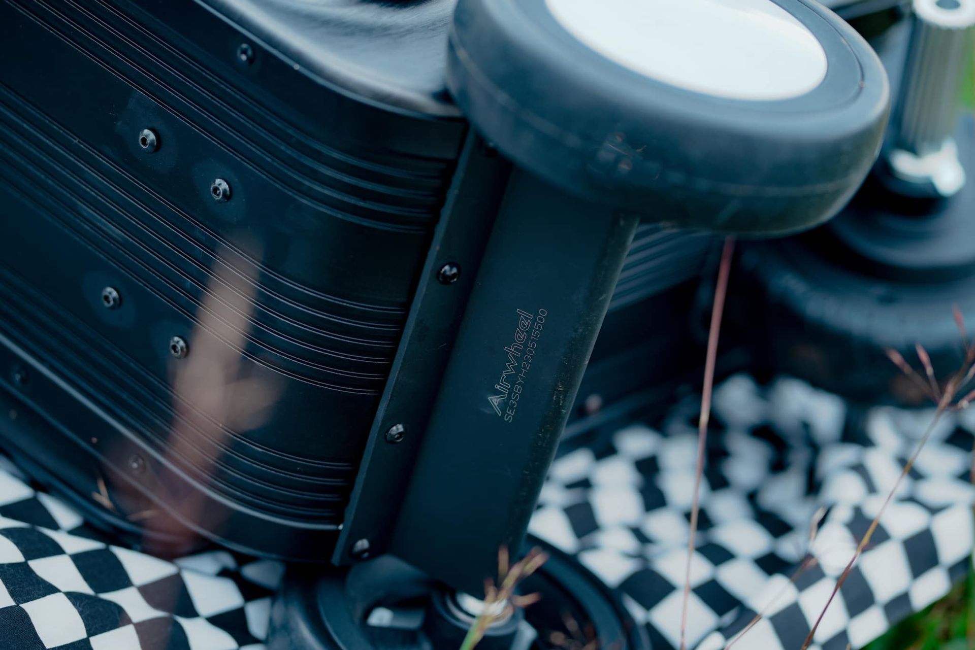 A black stroller is sitting on top of a checkered blanket.