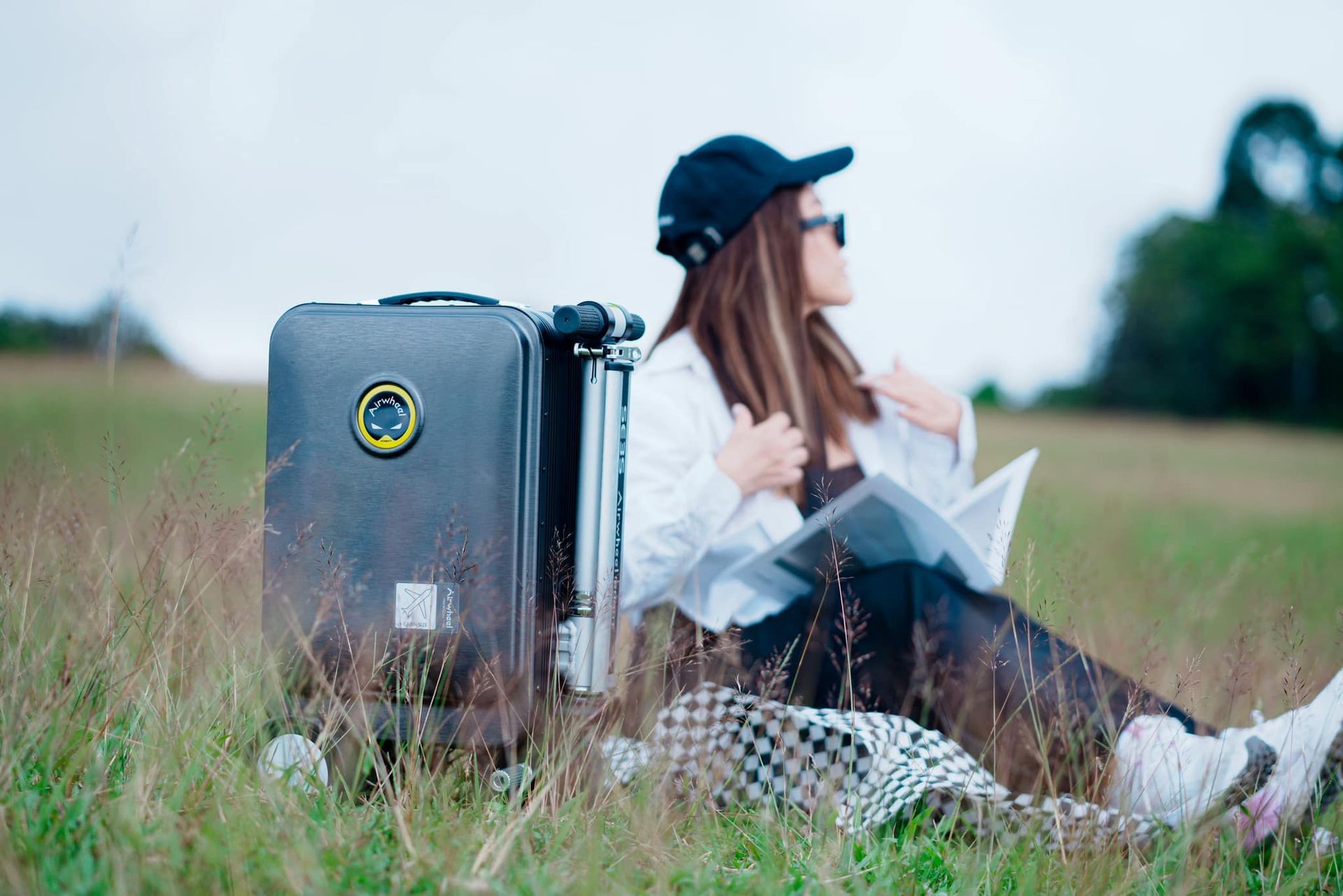 A woman is sitting in a field with a suitcase and a map.