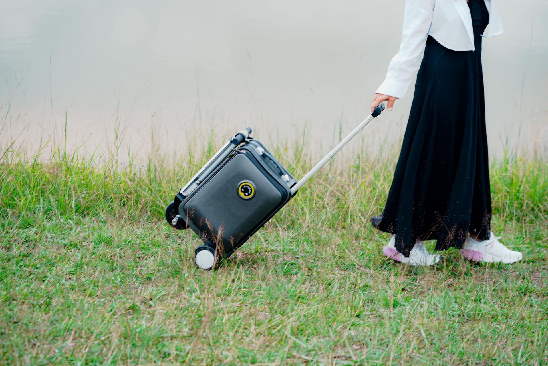 A woman is pulling a suitcase on wheels in the grass.