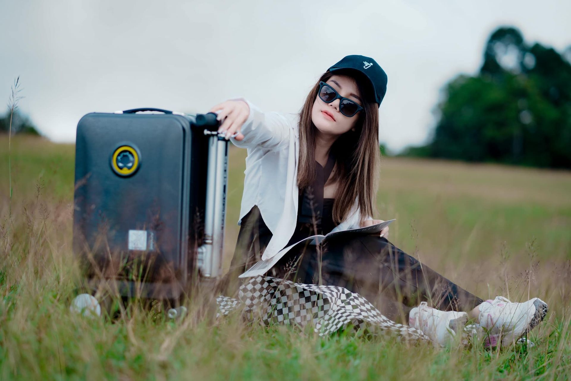A woman is sitting in the grass next to a suitcase.