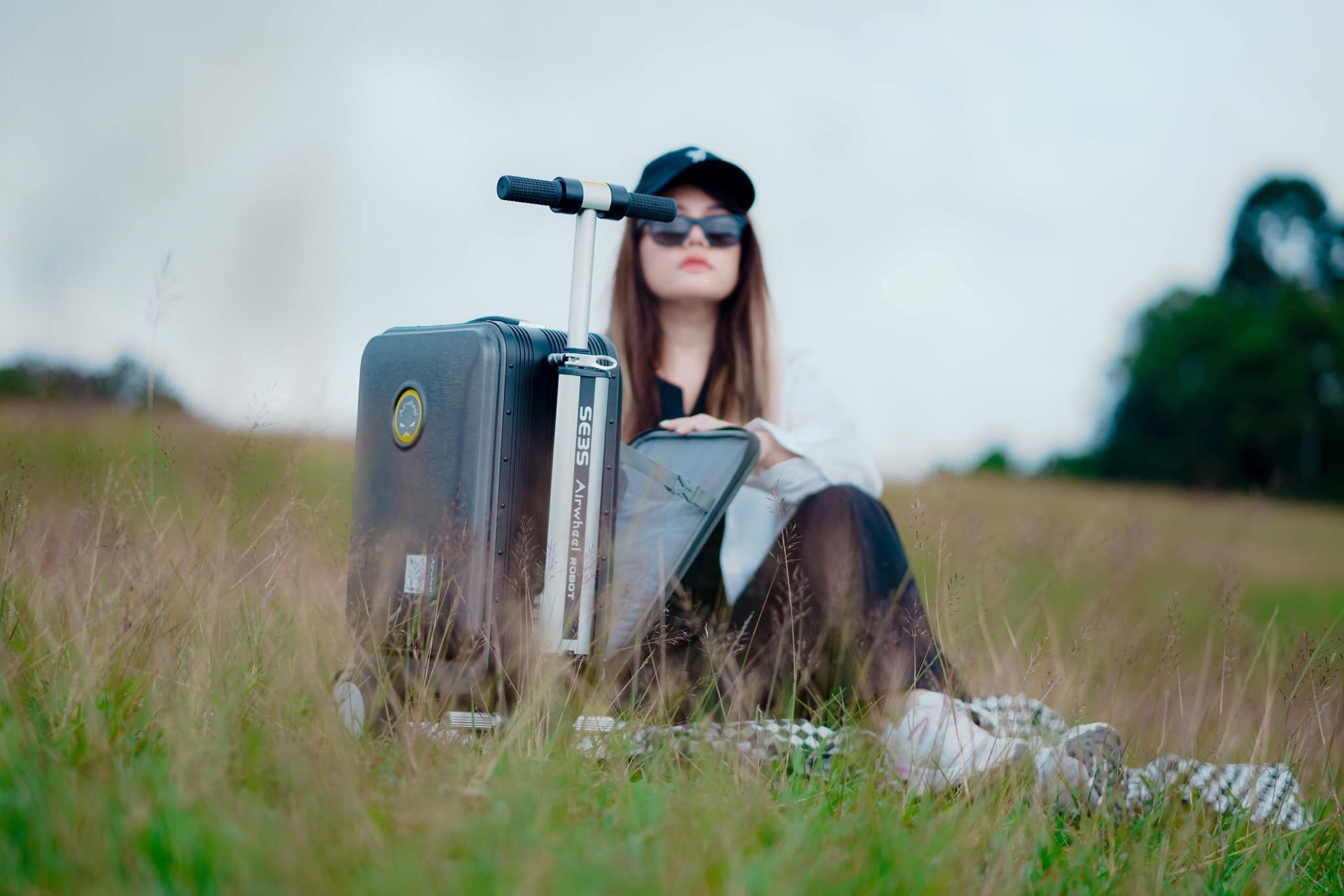 A woman is sitting in the grass with a suitcase.