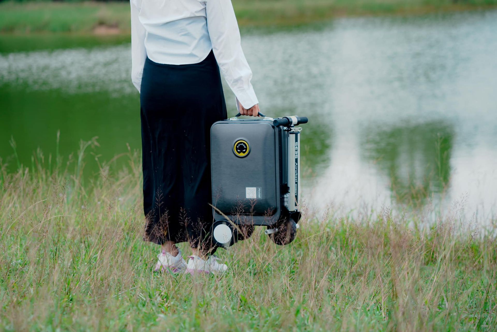 A woman is standing in a field holding a suitcase.