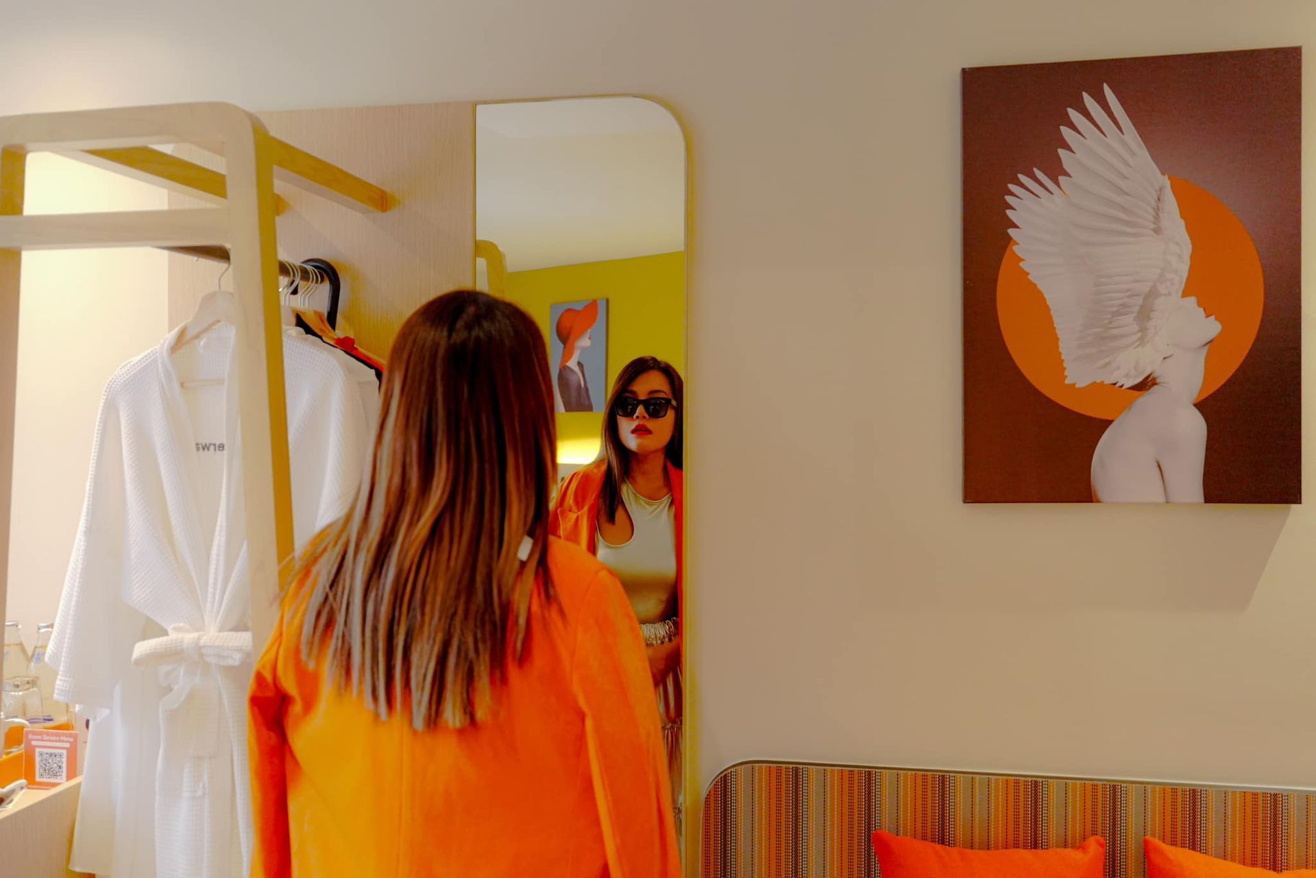A woman is looking at herself in a mirror in a Lumen hotel room.