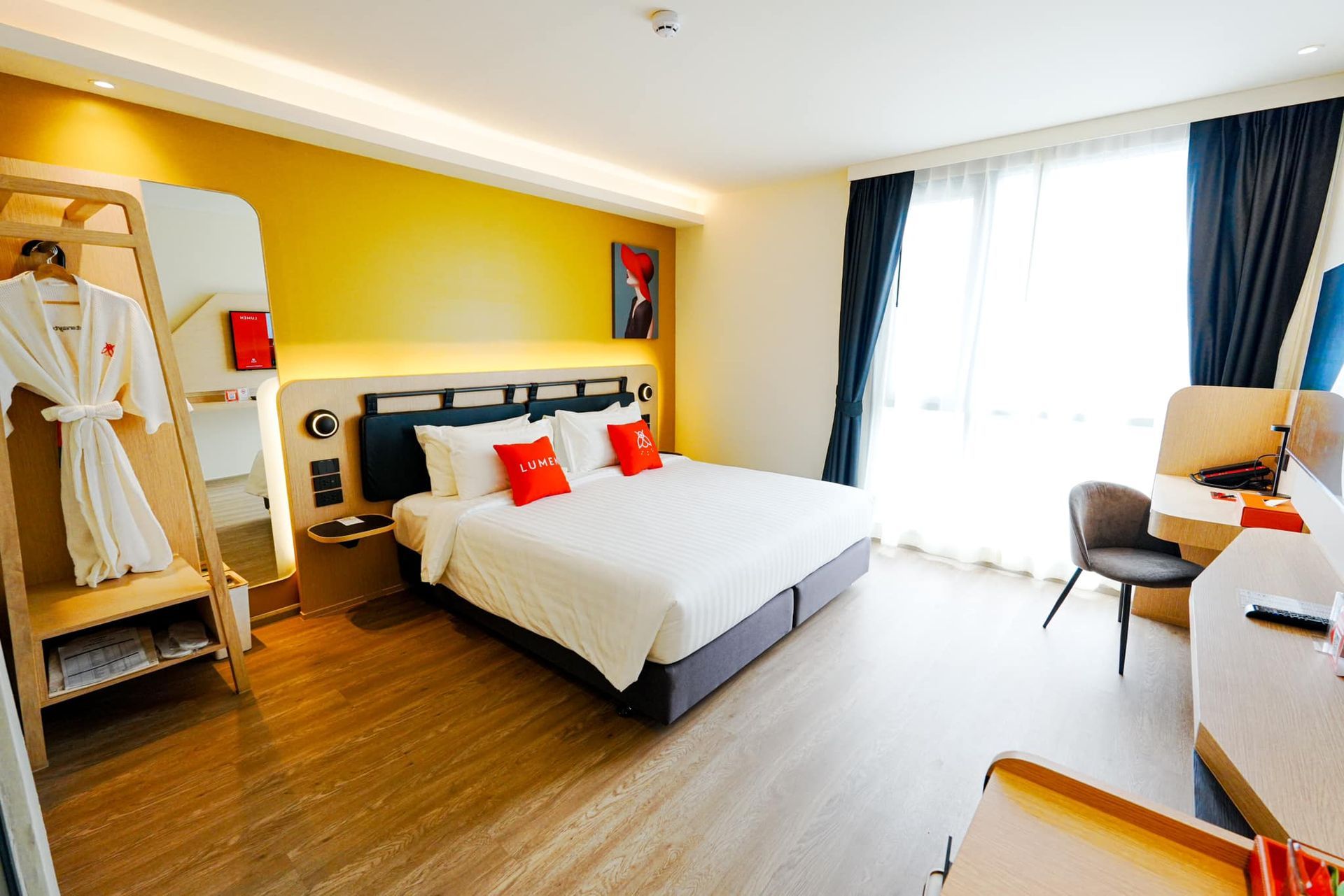 A hotel room with a king size bed , desk , chair and mirror in Lumen Hotel.