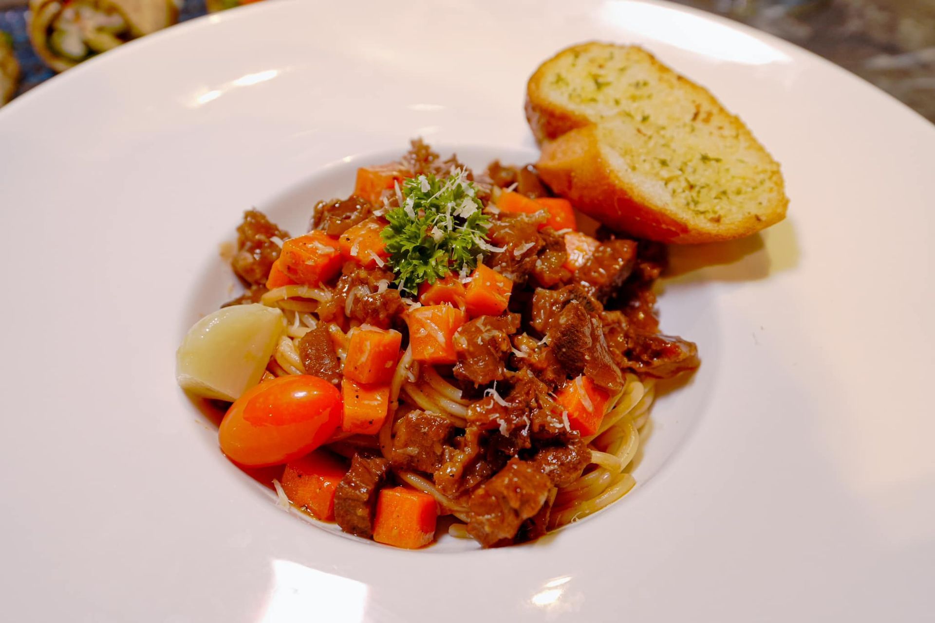 A white plate topped with spaghetti , meat , carrots and garlic bread.
