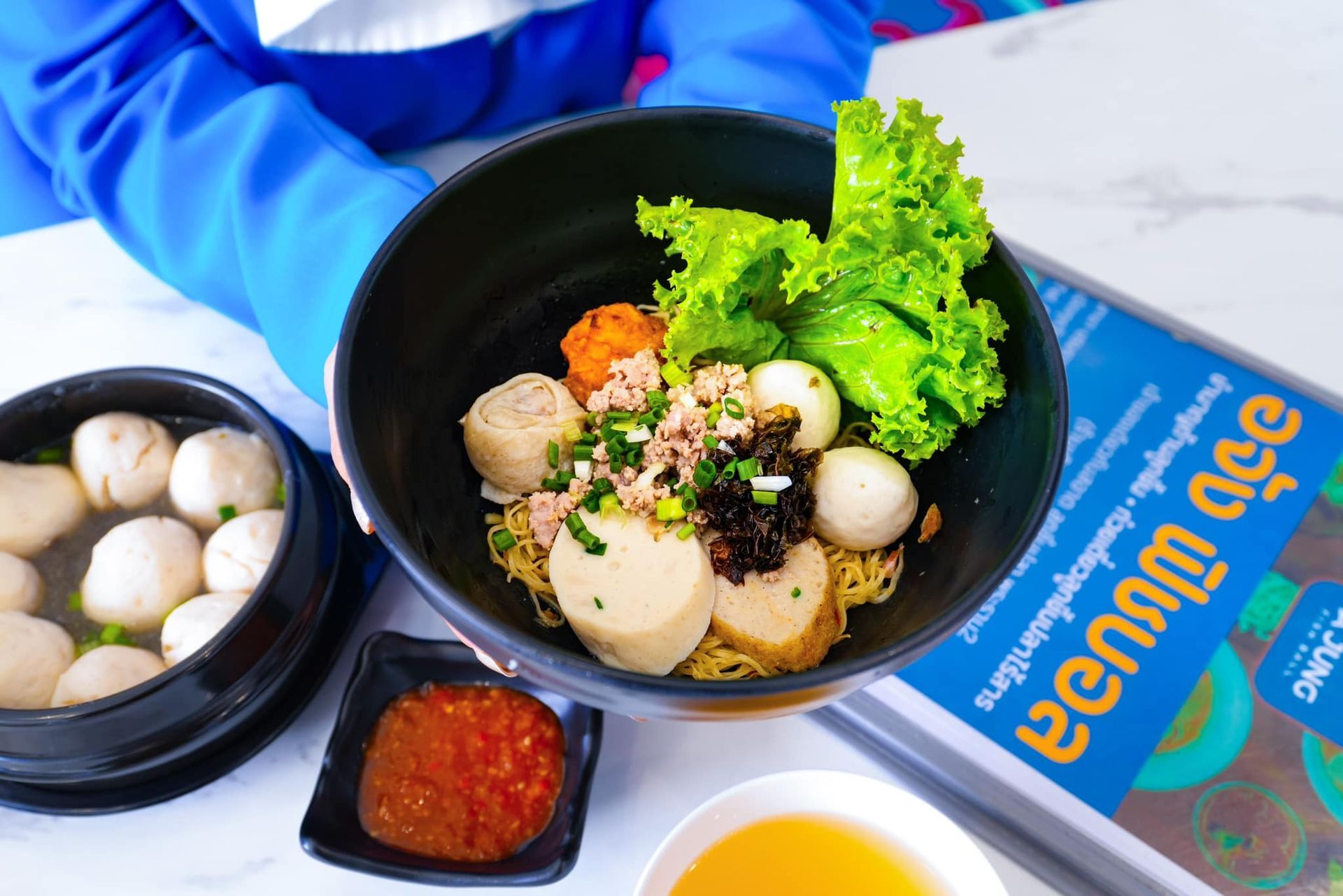 A person is sitting at a table with a bowl of noodles and fishballs.