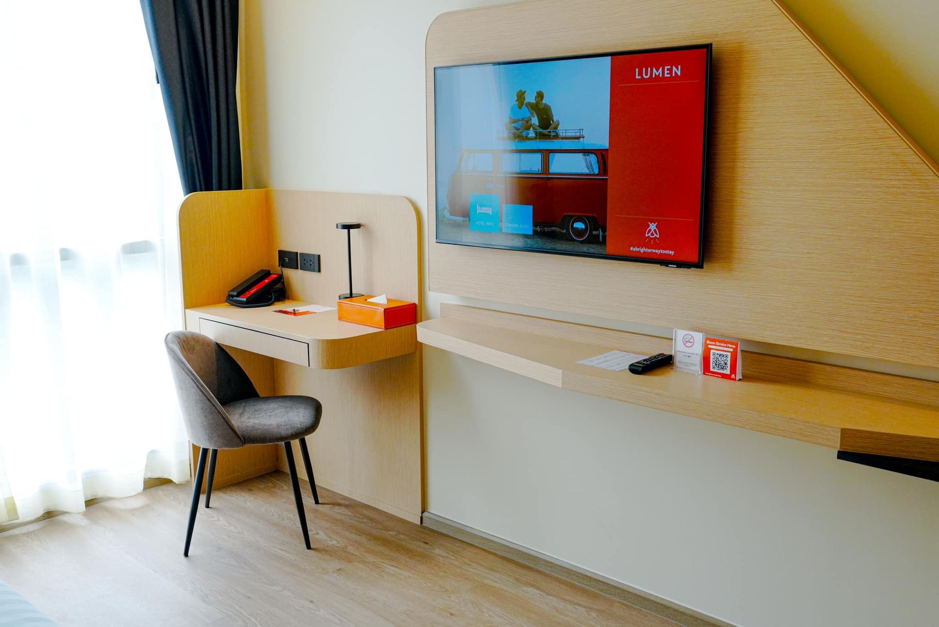 A hotel room with a desk and chair and a flat screen tv on the wall.