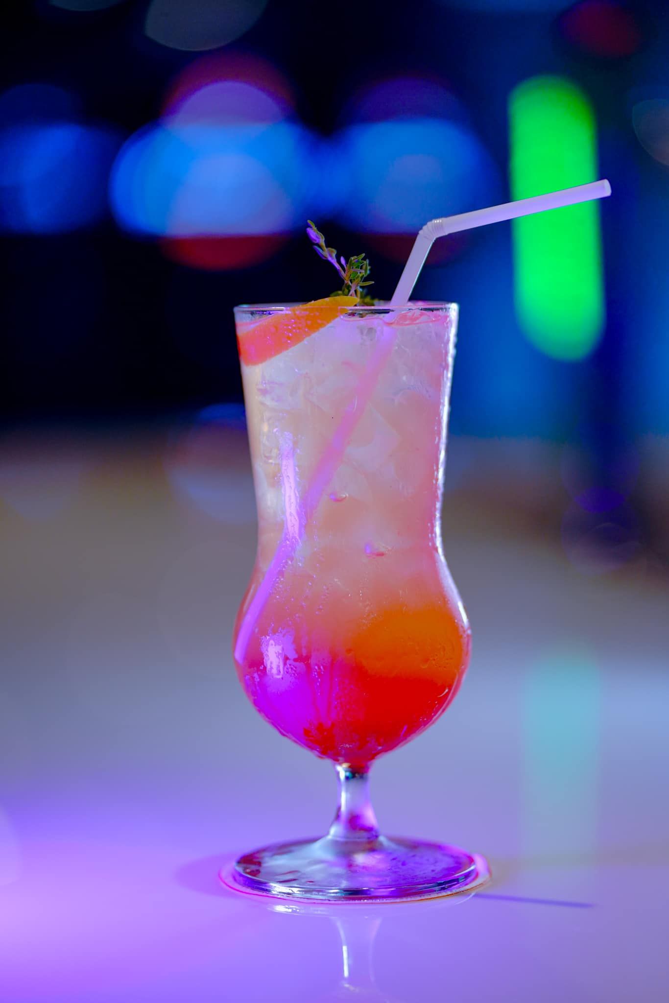 A close up of a colorful cocktail in a glass with a straw.