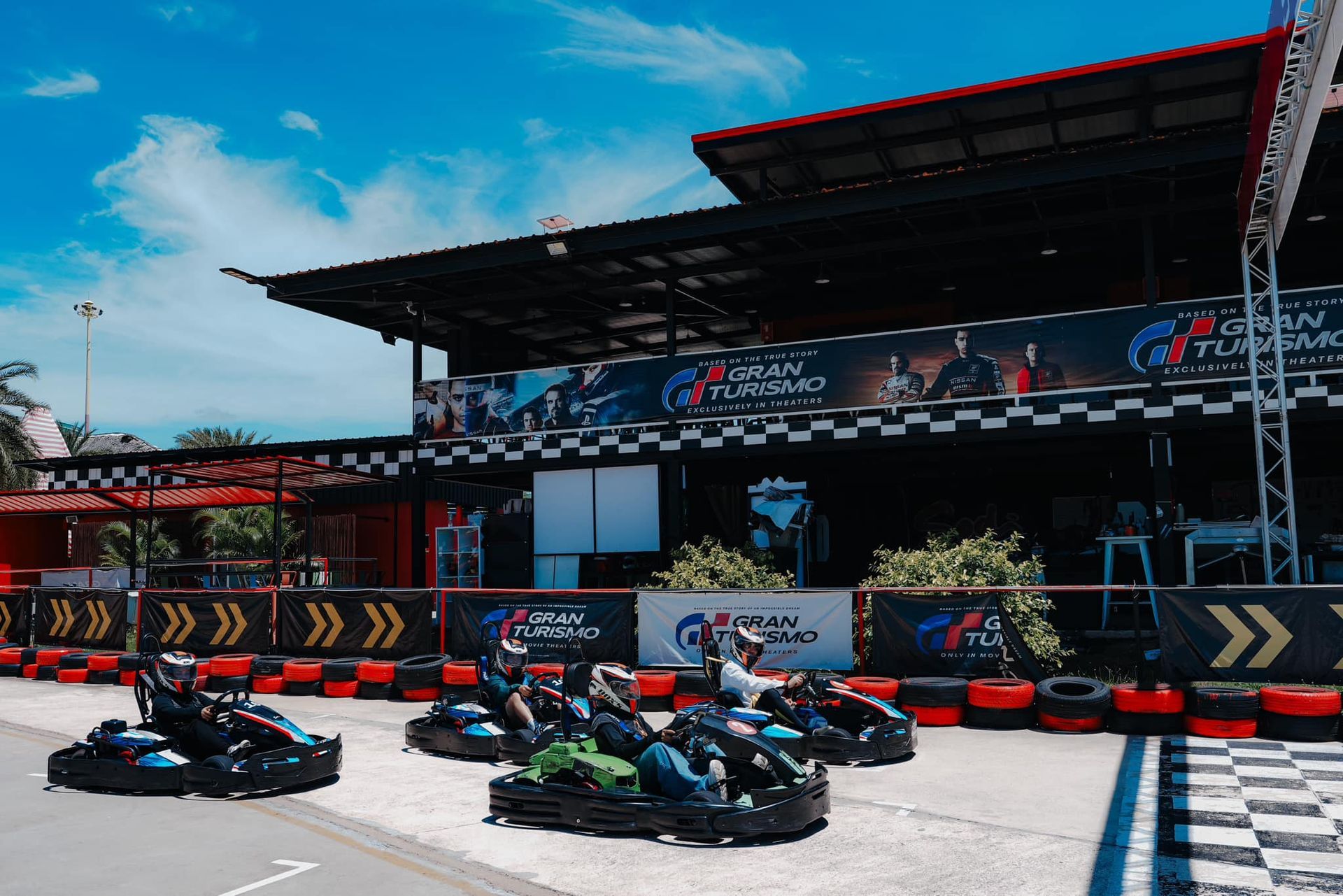 A group of people are riding go karts in front of a building that says gran turismo