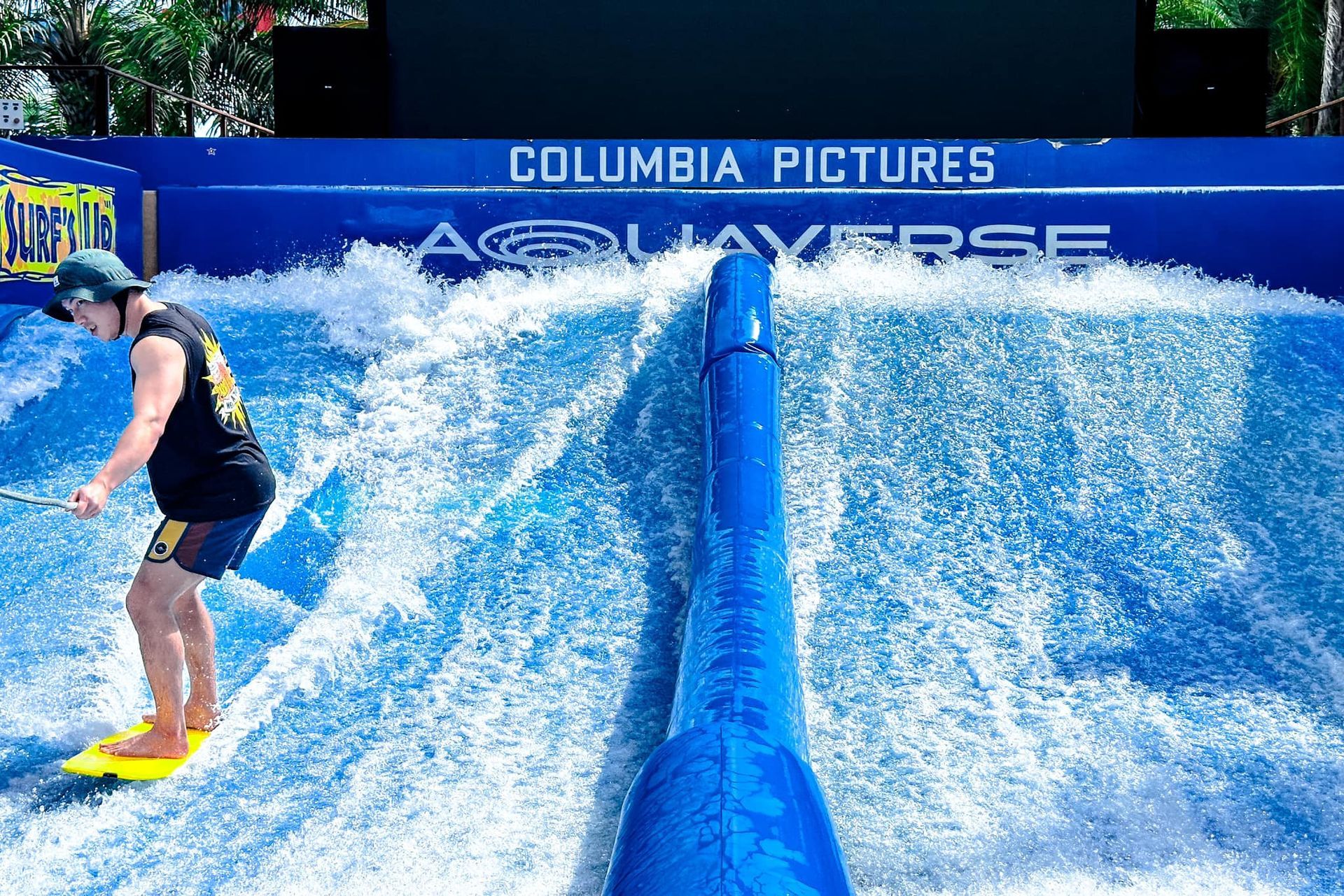 A man is riding a wave on a surfboard in front of a sign that says columbia pictures