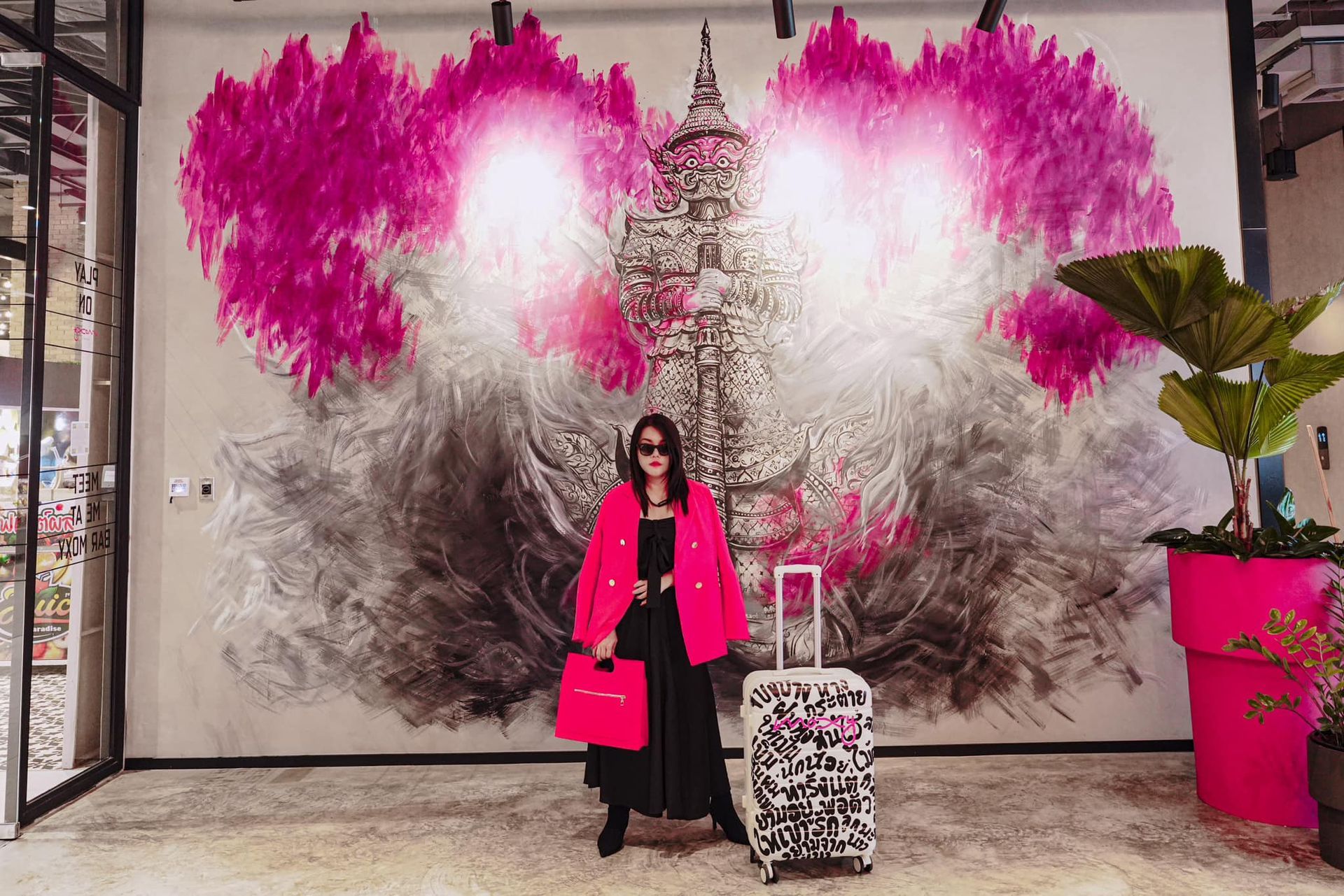 A woman is standing in front of a mural with a suitcase.