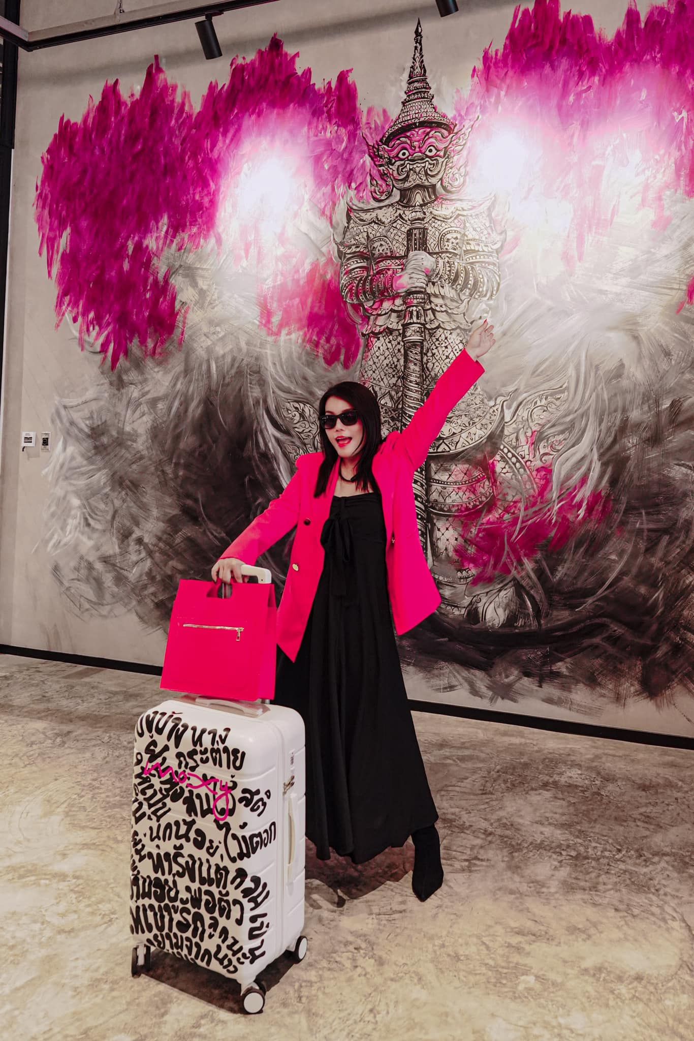 A woman in a pink jacket is standing next to a pink suitcase.