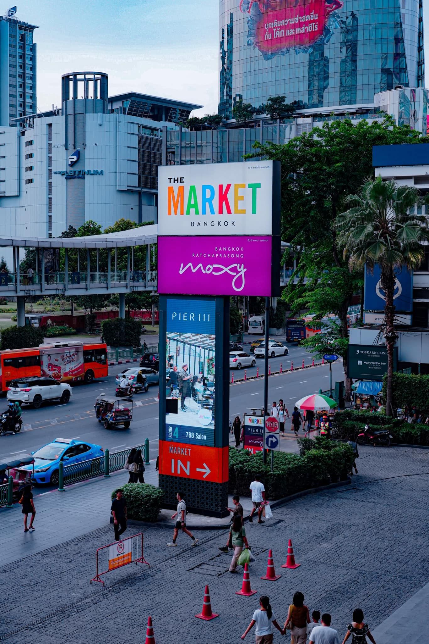 People are walking in front of a sign that says in Moxy Bangkok Ratchaprasong hotel.