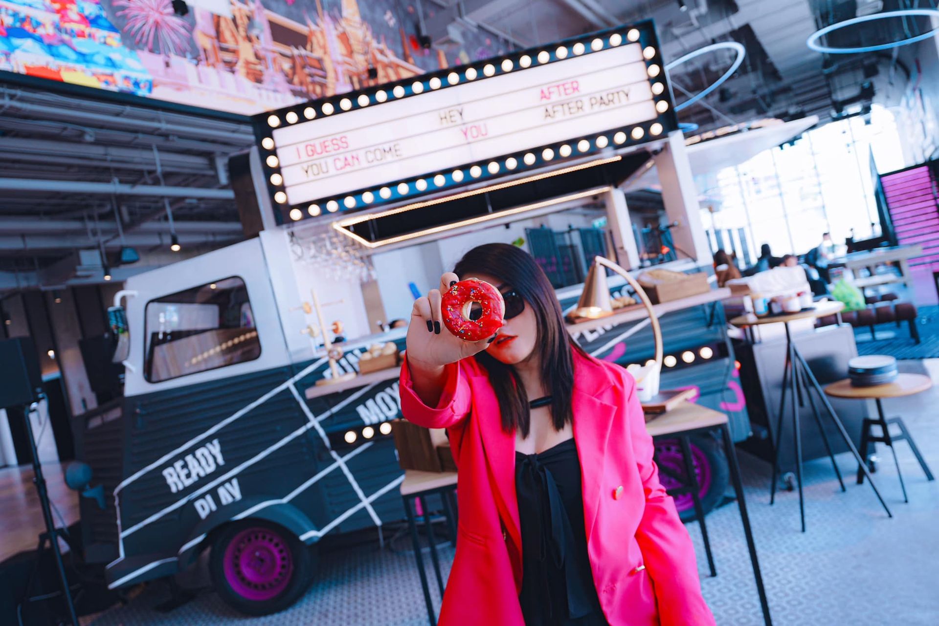 A woman in a pink jacket is holding a donut in front of her face.