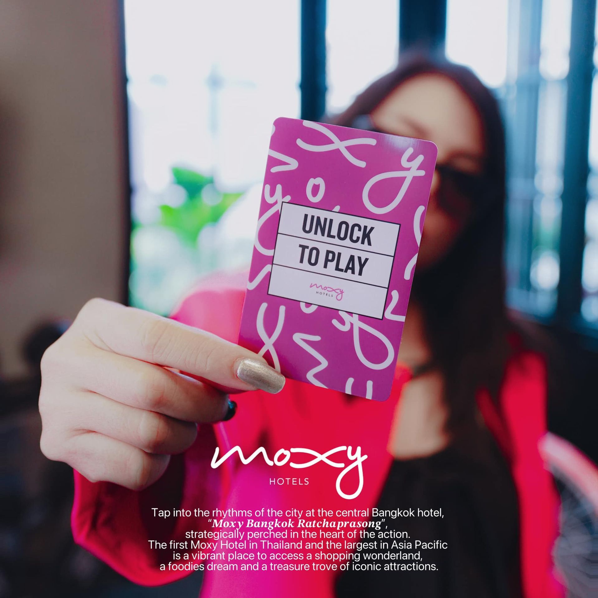A woman is holding a card that says unlock to play by Moxy hotel