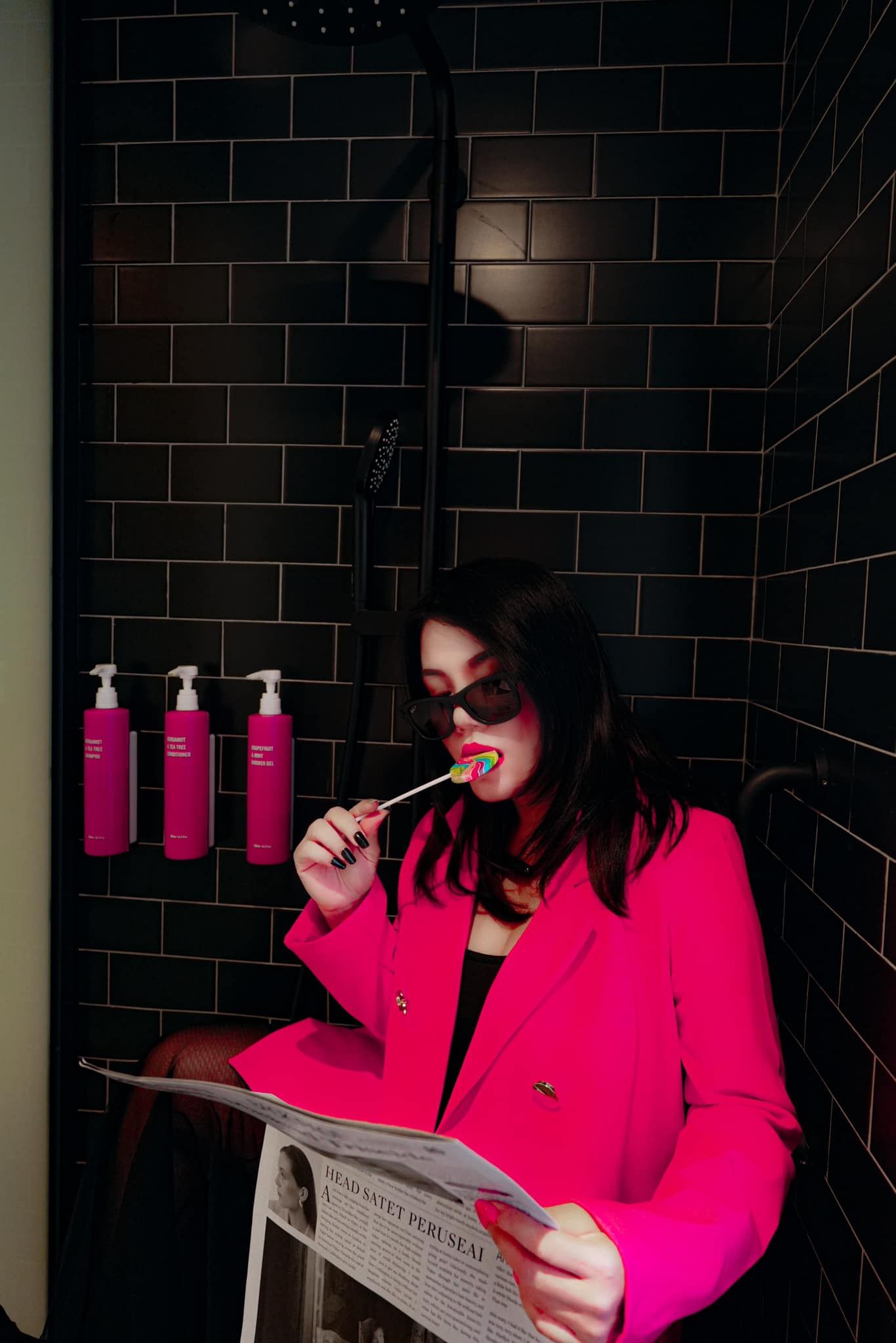 A woman in a pink jacket is brushing her teeth while reading a newspaper.