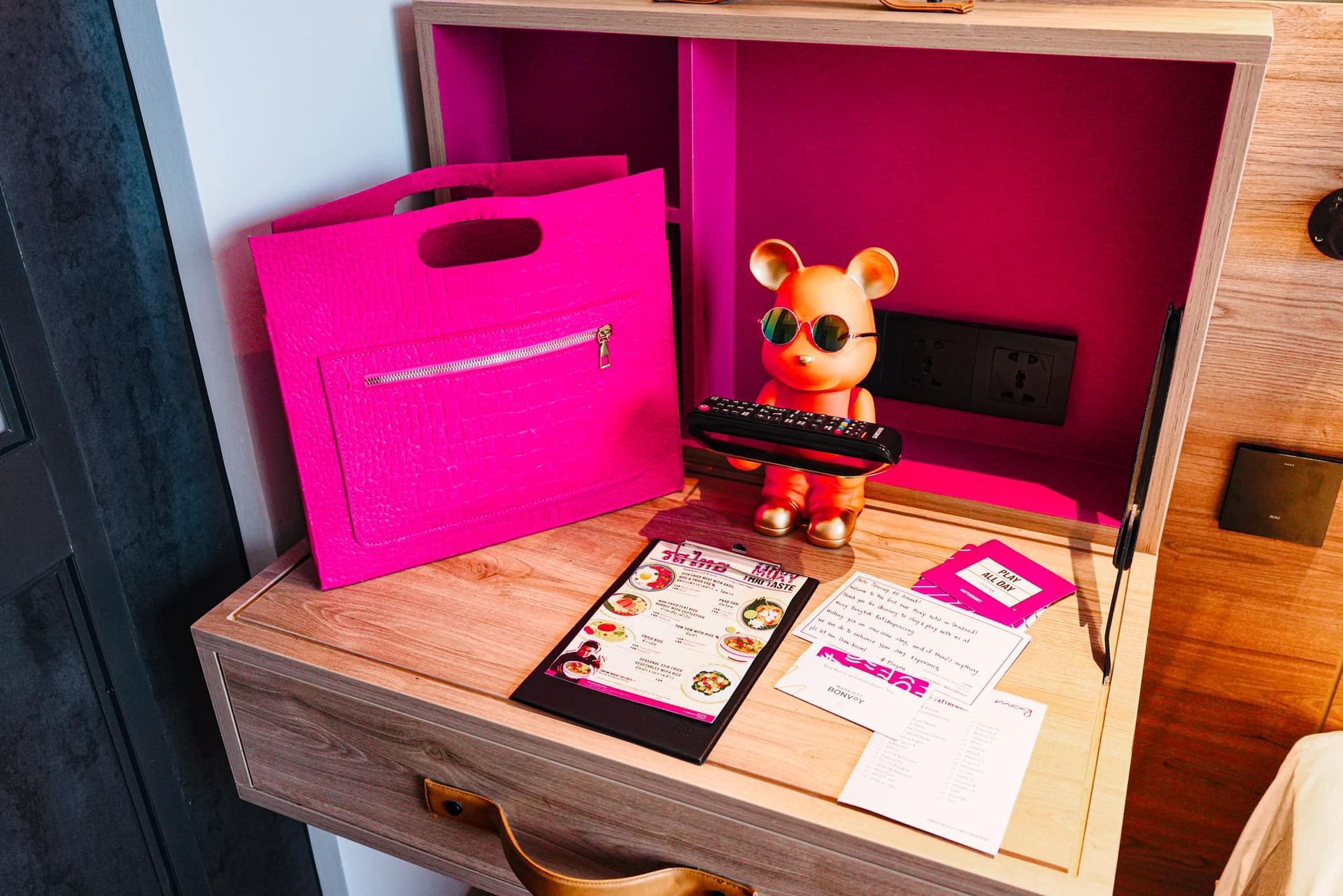 A wooden desk with a pink bag and a pink teddy bear on it.