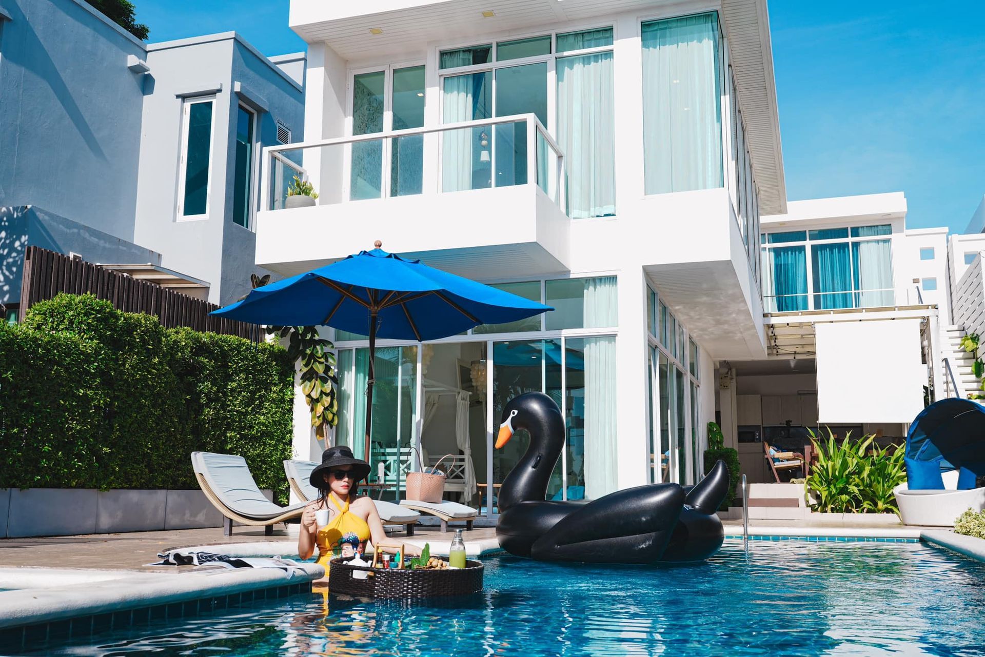 A woman is sitting on a swan float in a swimming pool in front of a house.