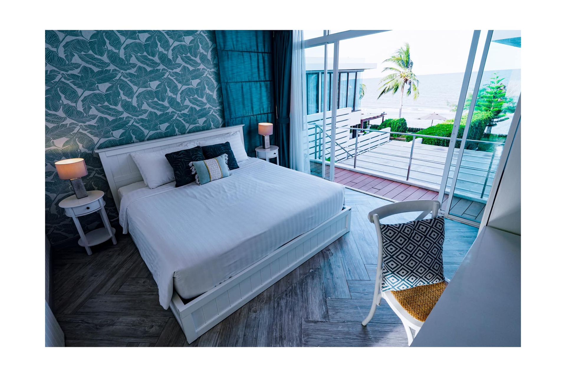 A bedroom with a large bed , chair , lamps and a view of the ocean.