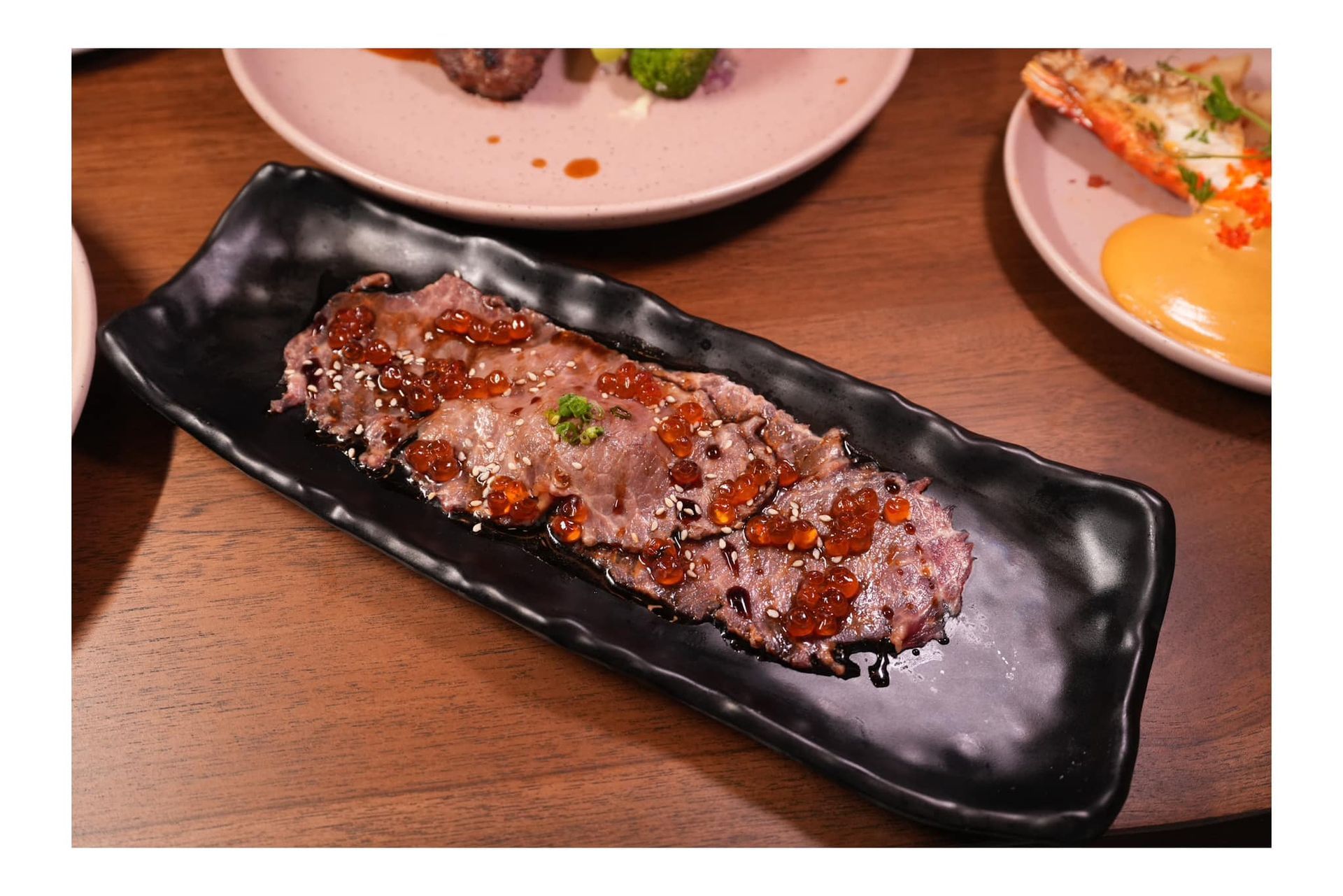 A piece of meat is on a black plate on a wooden table.