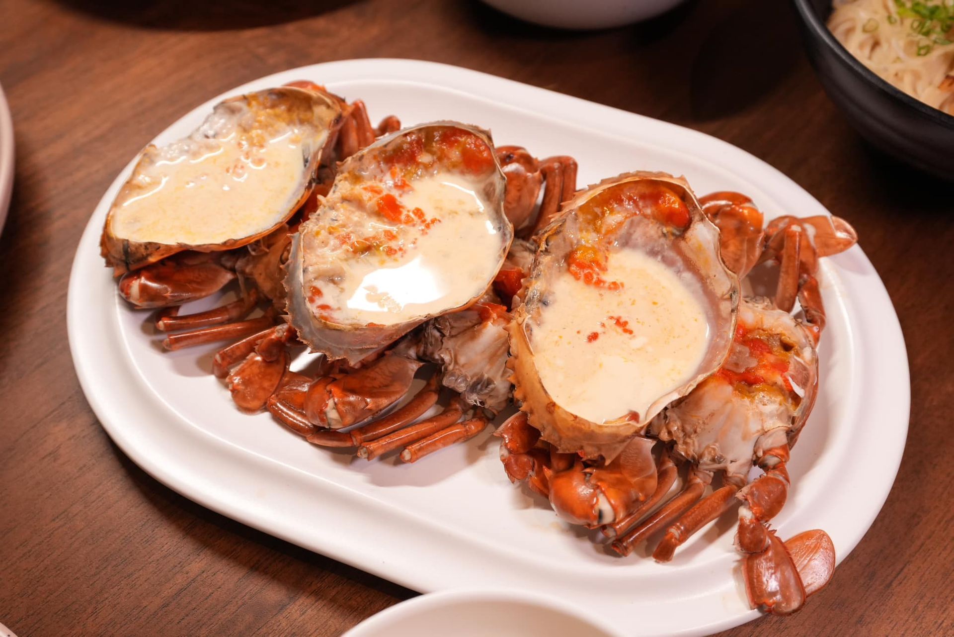 A white plate topped with three crabs on a wooden table. ปูไข่นึ่งนมสด