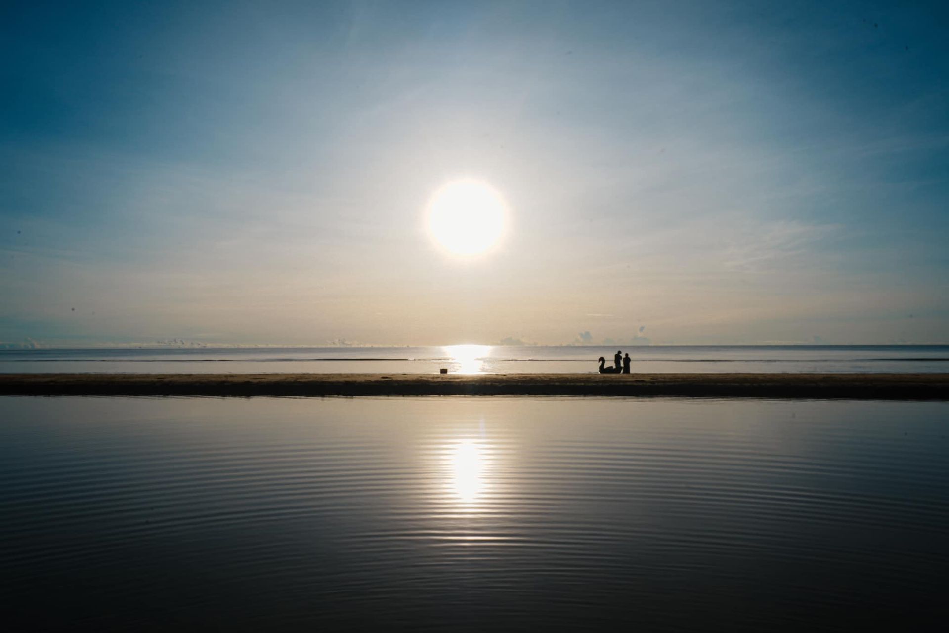 A couple standing on a beach watching the sun set over the ocean.