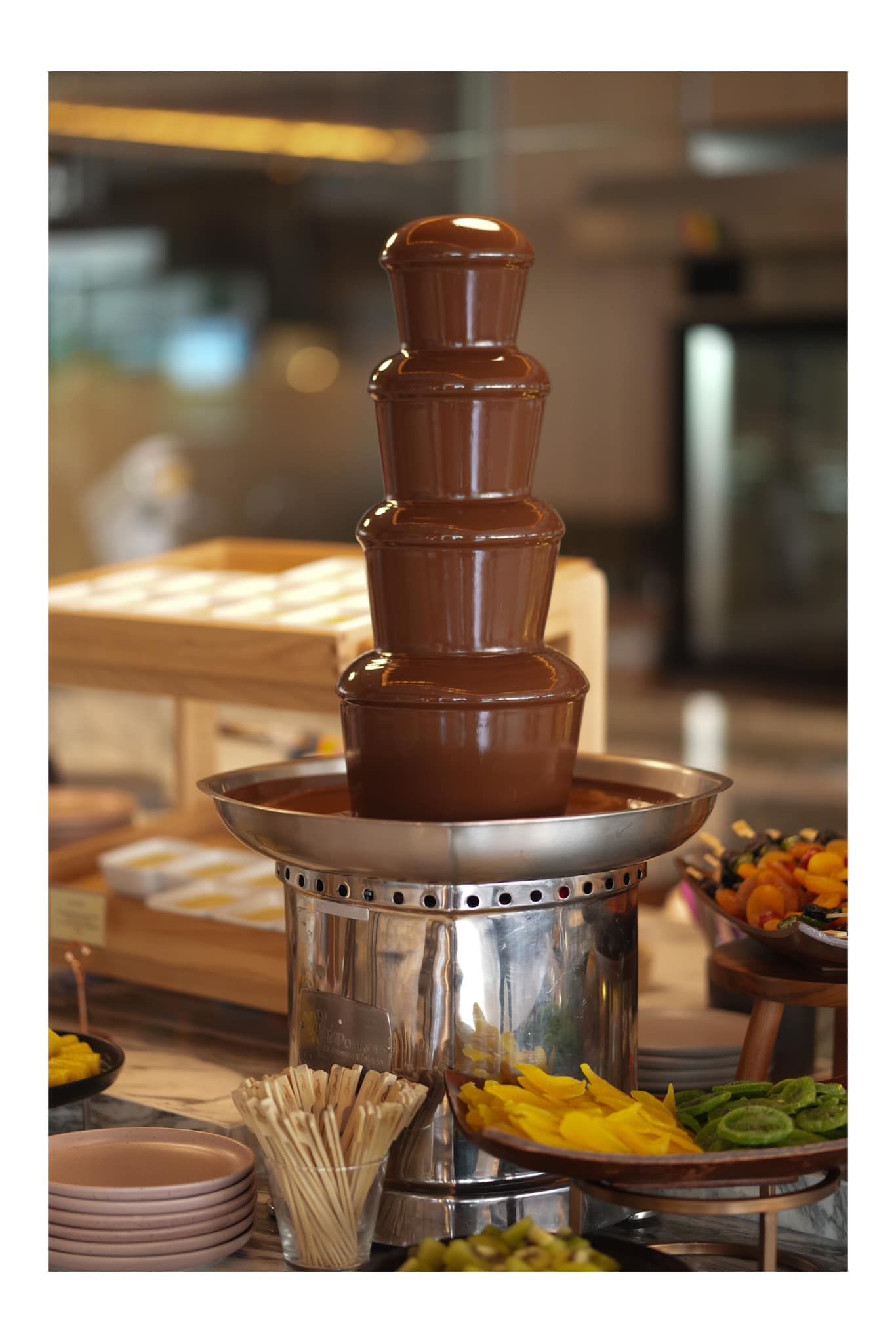 A chocolate fountain is sitting on top of a buffet table  at Atrium Restaurant.