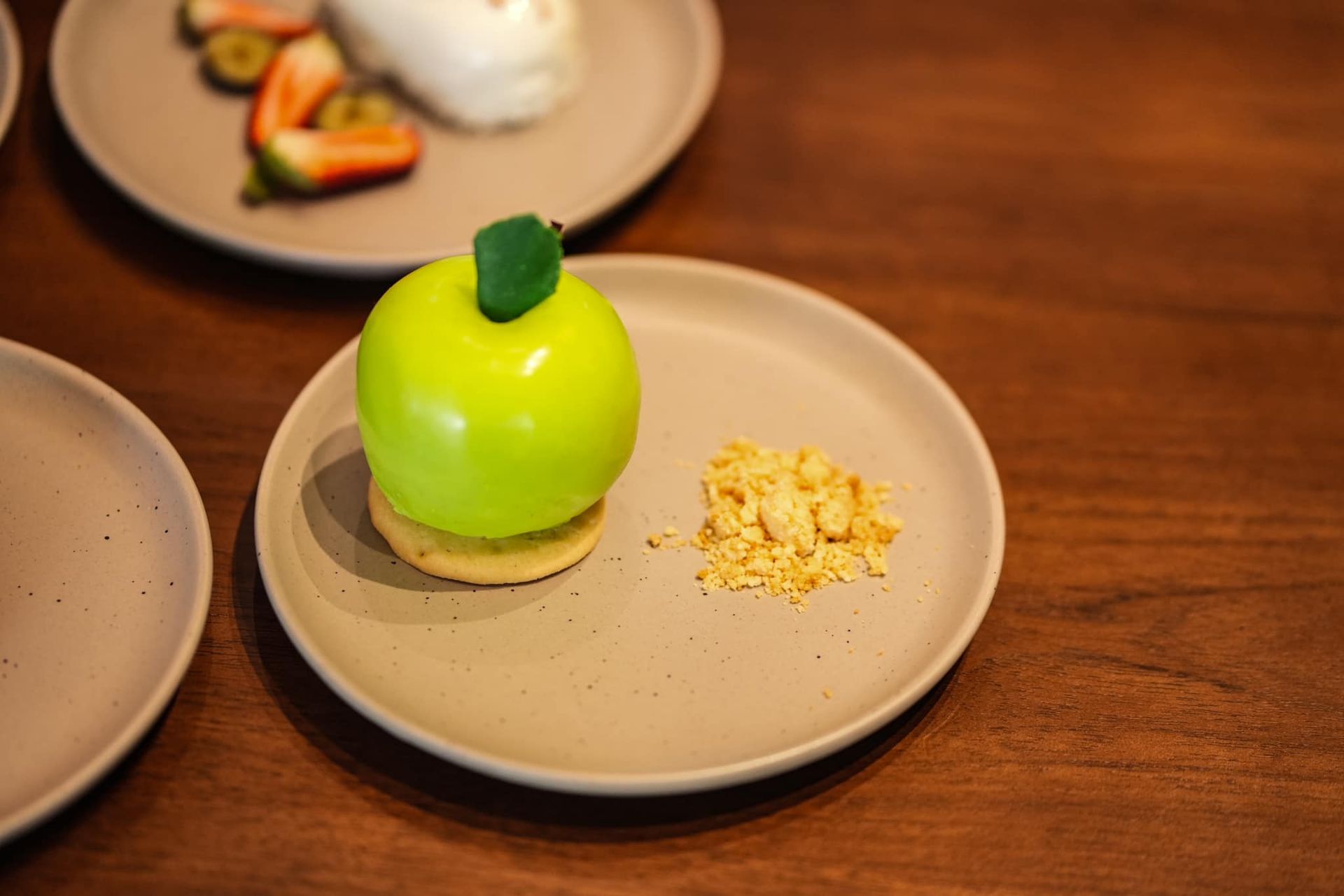 A green apple shaped dessert on a plate on a wooden table.