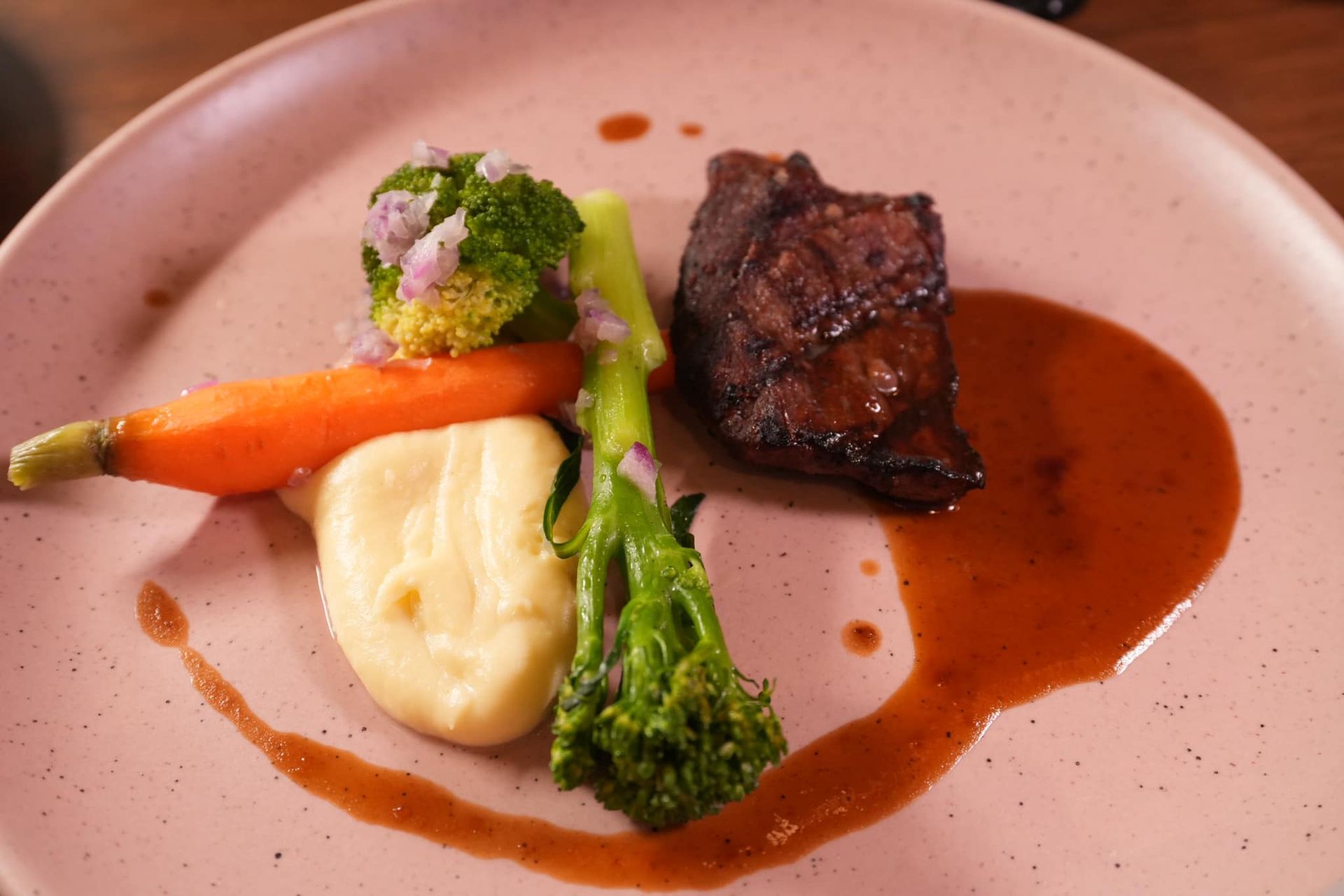 A plate of food with meat , broccoli , carrots and mashed potatoes on a table.