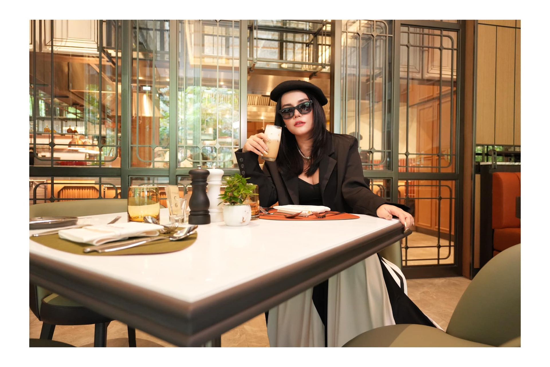 A woman is sitting at a table in a Atrium restaurant holding a cup of coffee.