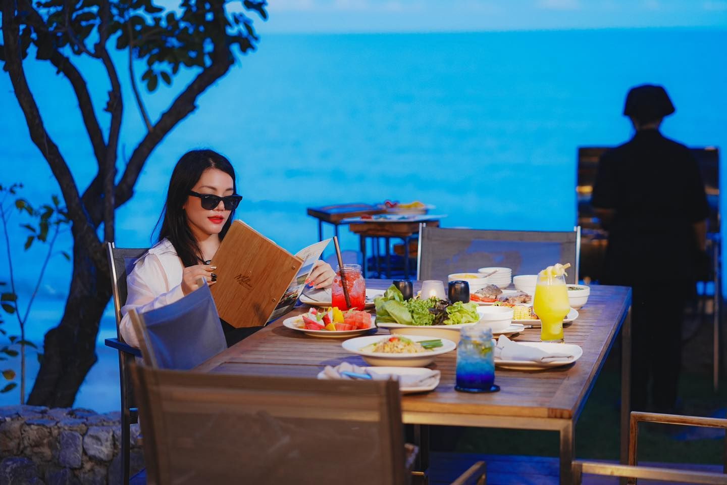 A woman is sitting at a table with a menu in front of the ocean.