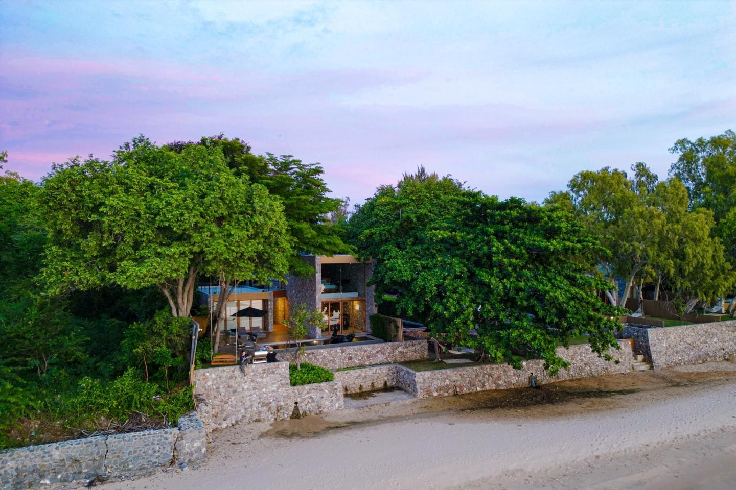 An aerial view of a house surrounded by trees on a beach.