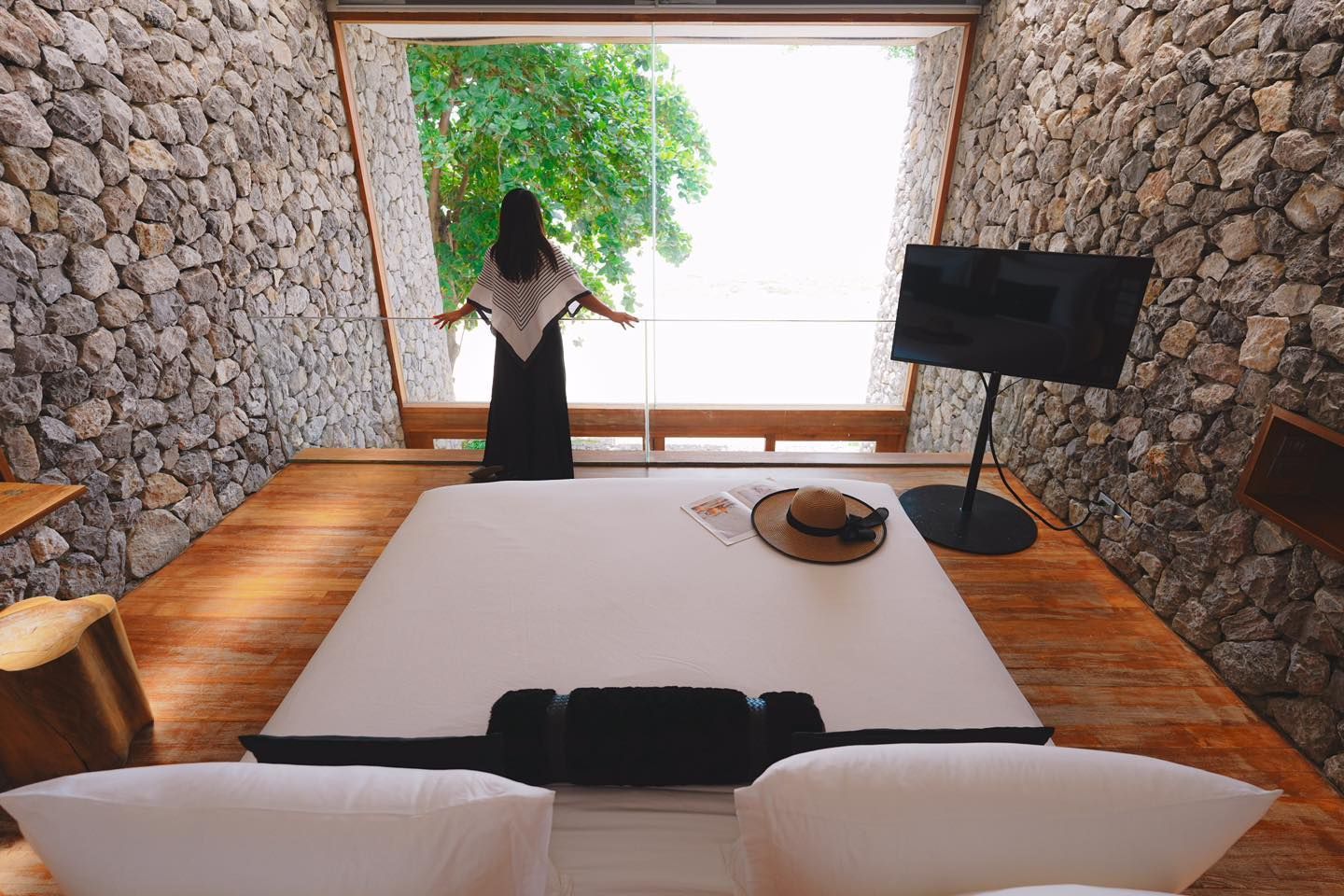 A woman is standing in a bedroom next to a bed and a television.
